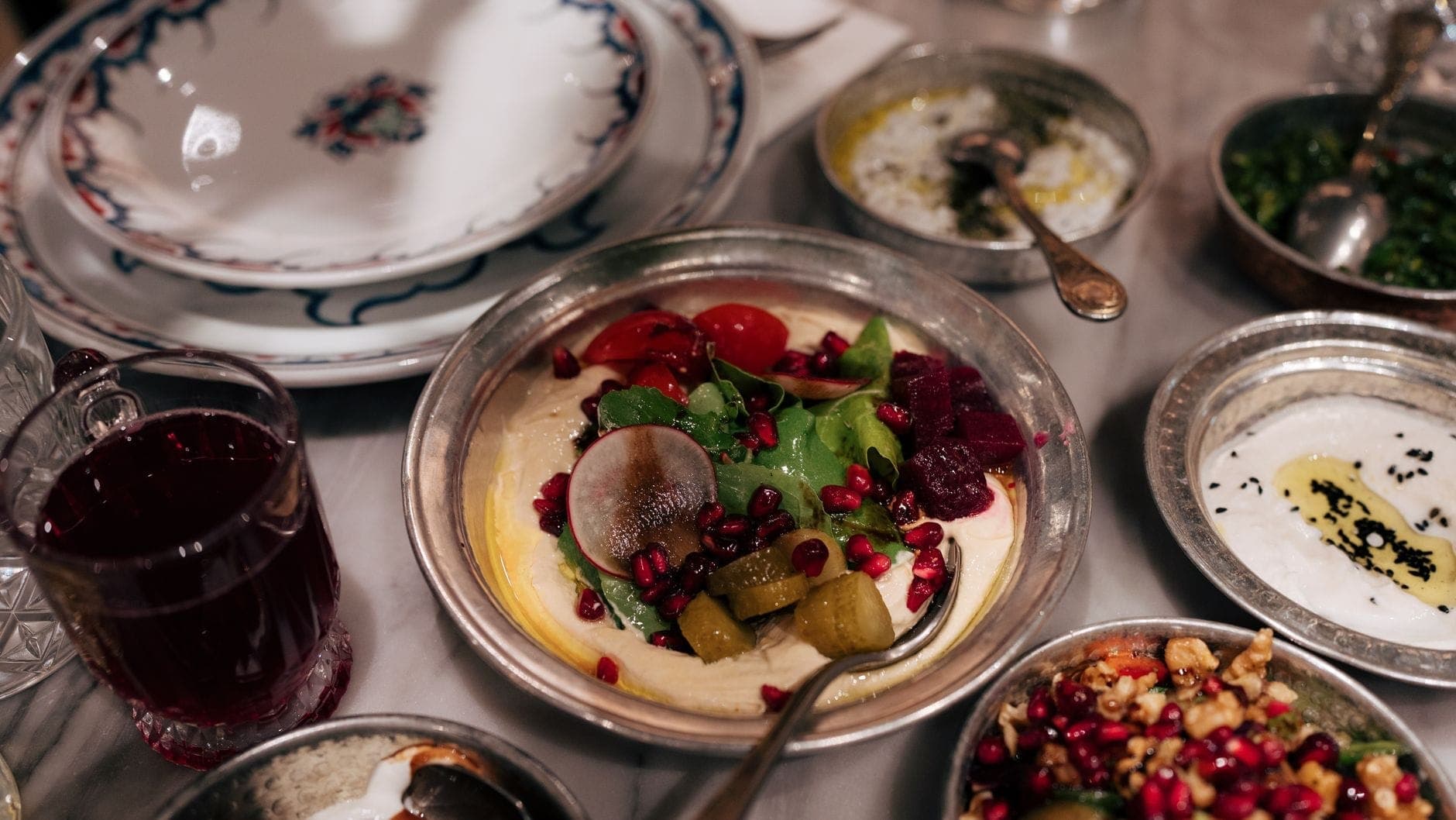 Eine Auswahl bunter Meze-Gerichte in traditionellen Metallschälchen auf einem Marmortisch mit Gemüse, Granatapfelkernen und Pickles – authentisches türkisches Meyhane-Flair.