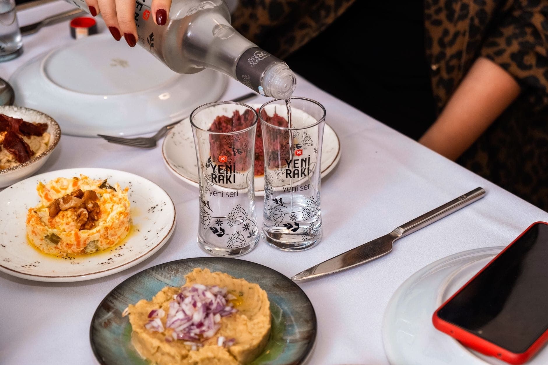 Ein gedeckter Tisch mit verschiedenen türkischen Meze-Gerichten und zwei eingeschenkten Gläsern Rakı, der eine klassische Meyhane-Szene in Istanbul einfängt.