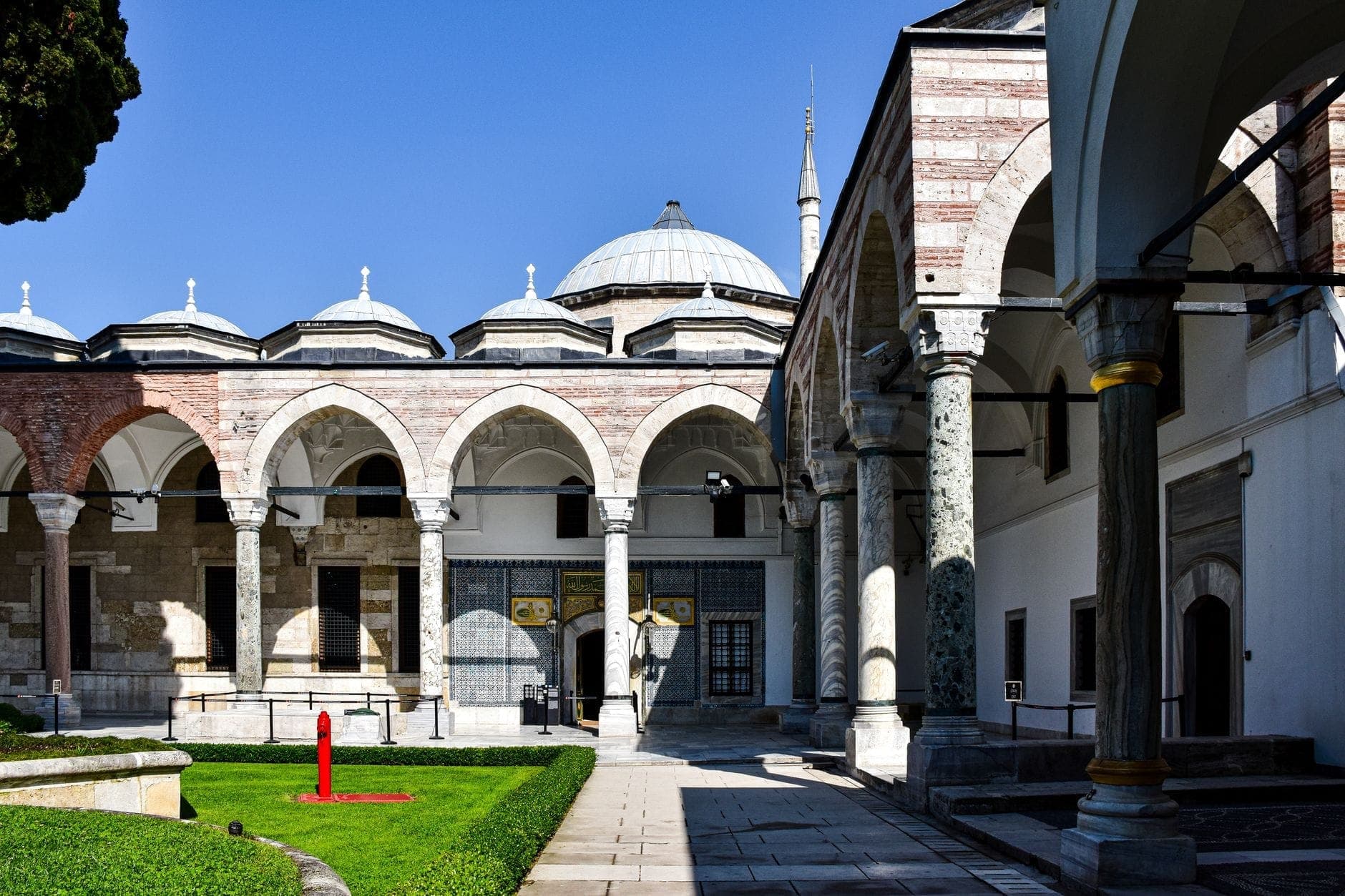 Pemandangan halaman yang cerah dengan kolonade berarkat dan atap berkubah di Istana Topkapi di Istanbul, situs utama yang termasuk dalam Museum Pass.