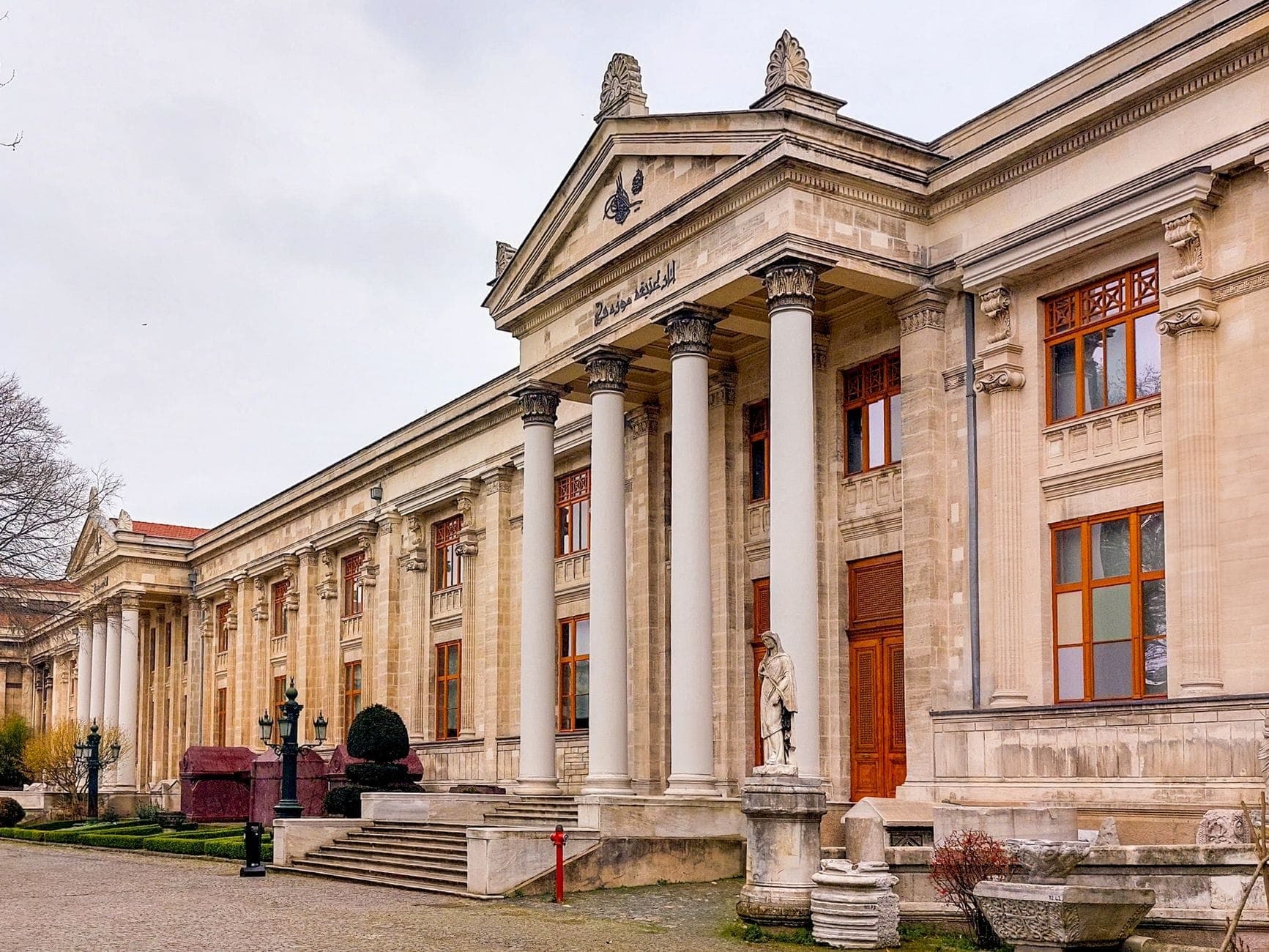 Tampilan sudut lebar pintu masuk utama Museum Arkeologi Istanbul dengan kolom neoklasik dan patung, situs utama dalam Museum Pass.