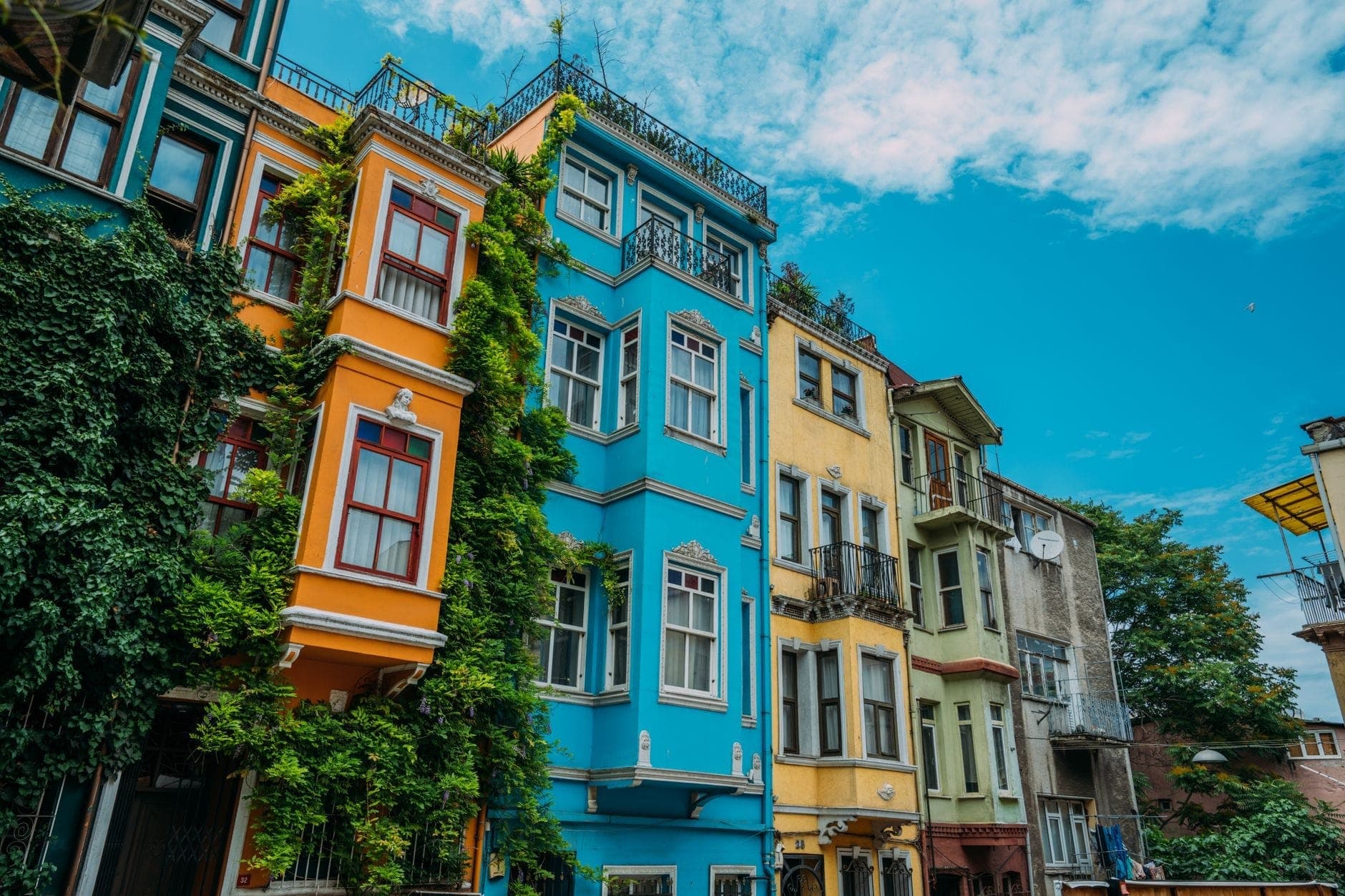 Edificios históricos de apartamentos multicolores en un vibrante barrio de Estambul bajo un cielo azul brillante, transmitiendo una sensación de opciones de alojamiento locales y económicas.