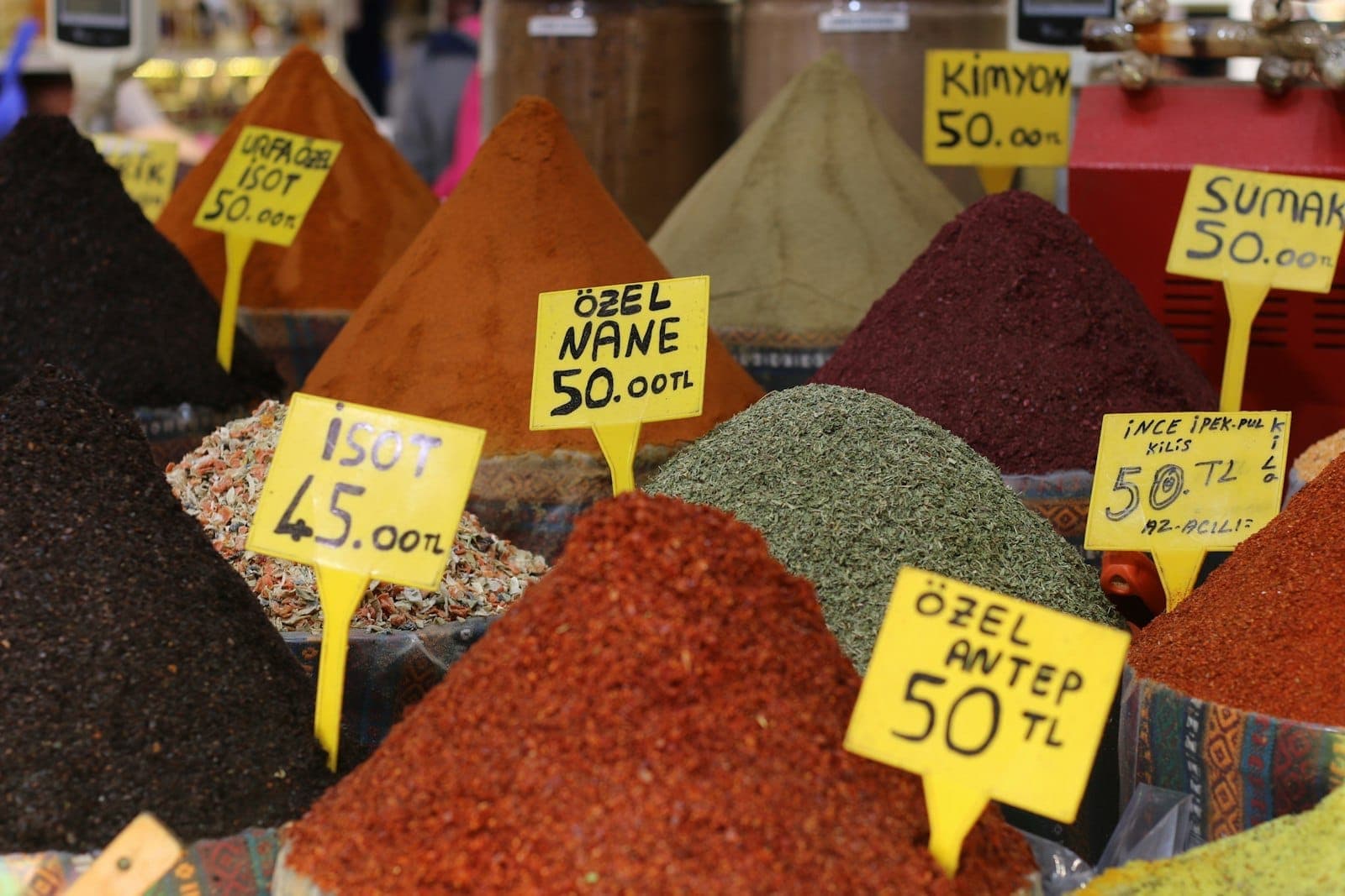 Tas colorés d'épices avec des panneaux en turc sur un étal de marché animé à Istanbul, évoquant la culture locale de la street food.