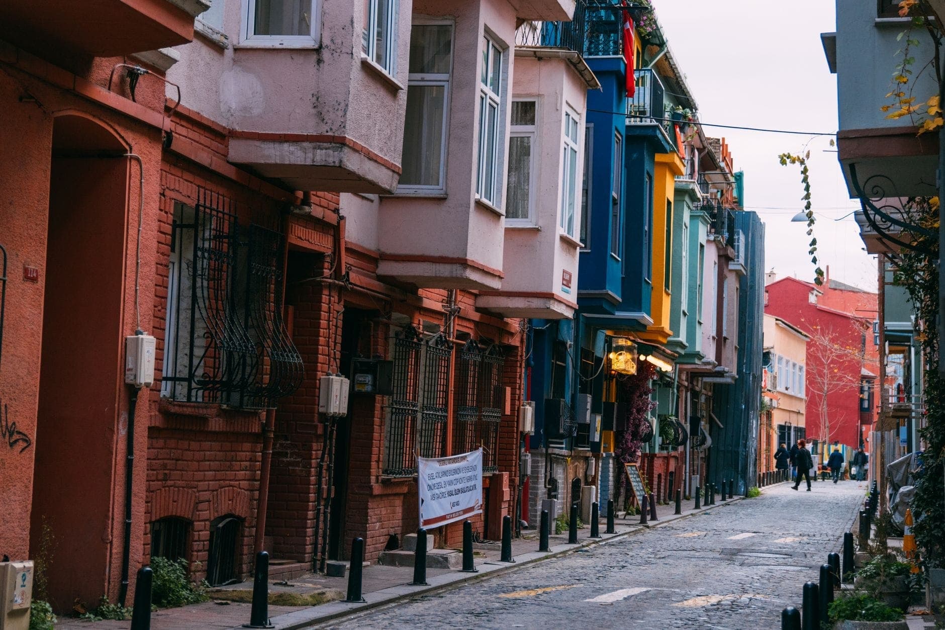 Bunte Häuser aus der osmanischen Ära in einer charmanten Straße im Viertel Fener und Balat in Istanbul, mit Menschen, die das Kopfsteinpflaster entlanggehen.