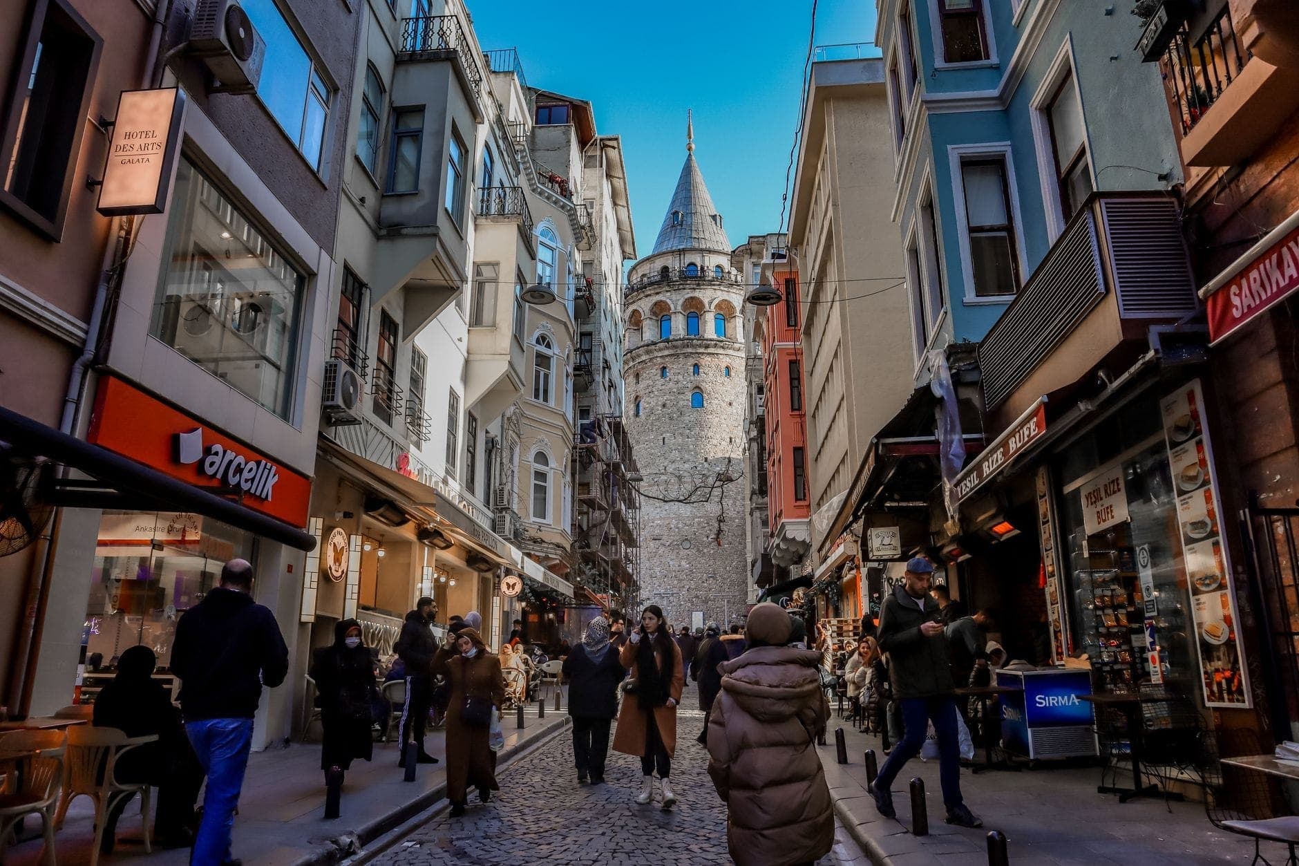 Blick eine lebhafte Straße entlang zum Galata-Turm, umgeben von bunten Gebäuden und Spaziergängern, stellvertretend für das Herz von Beyoğlu und Galata.
