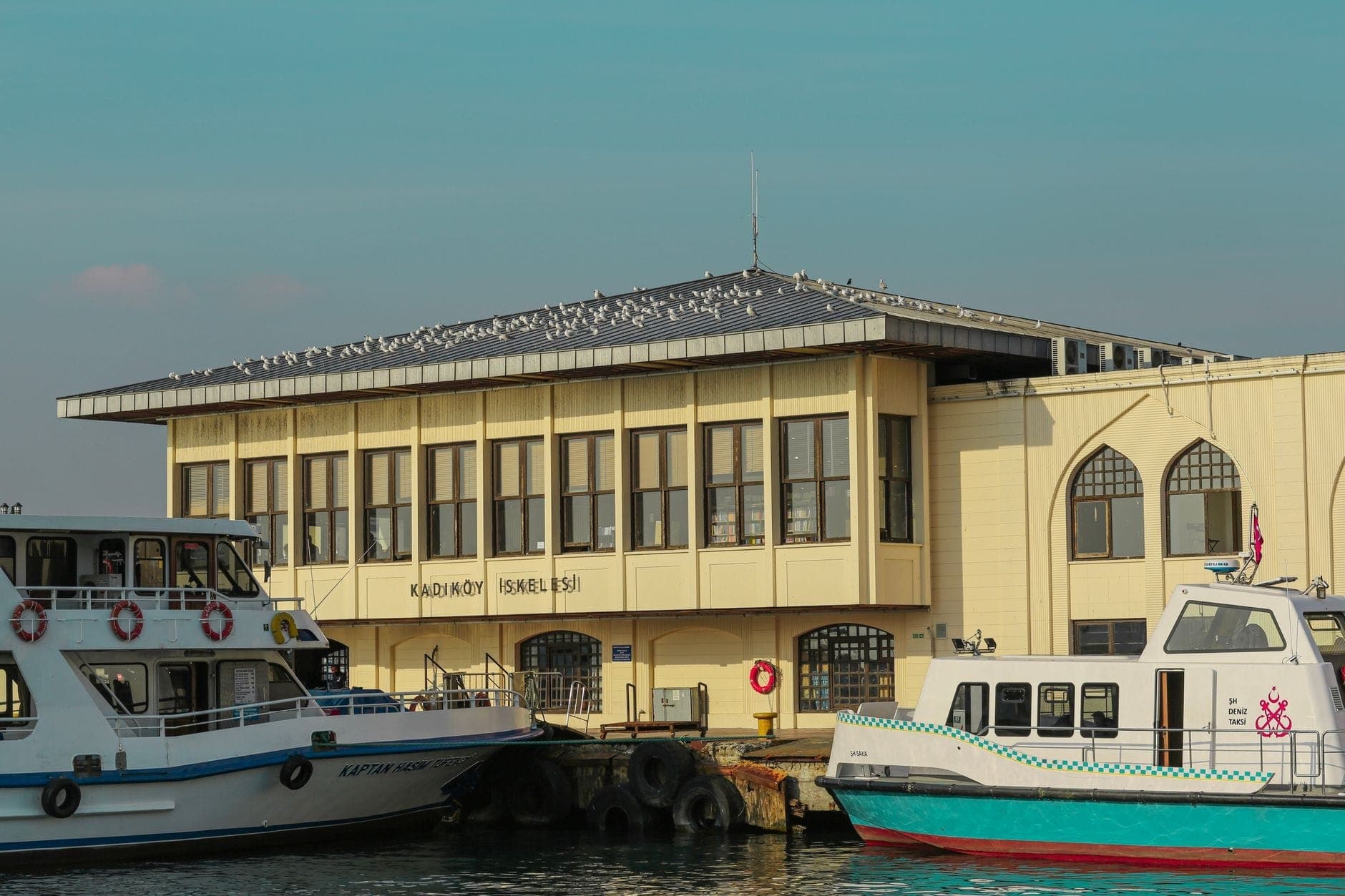 Fährterminal Kadıköy auf der asiatischen Seite Istanbuls mit angedockten Fähren und Möwen auf dem Dach unter einem klaren blauen Himmel.
