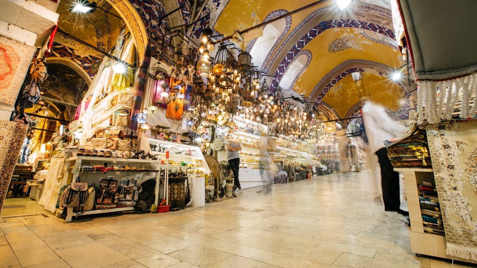 Weitwinkelansicht des Inneren des Großen Basars in Istanbul mit lebhaften Lampen, bunten Waren und gewölbten gelben Decken.