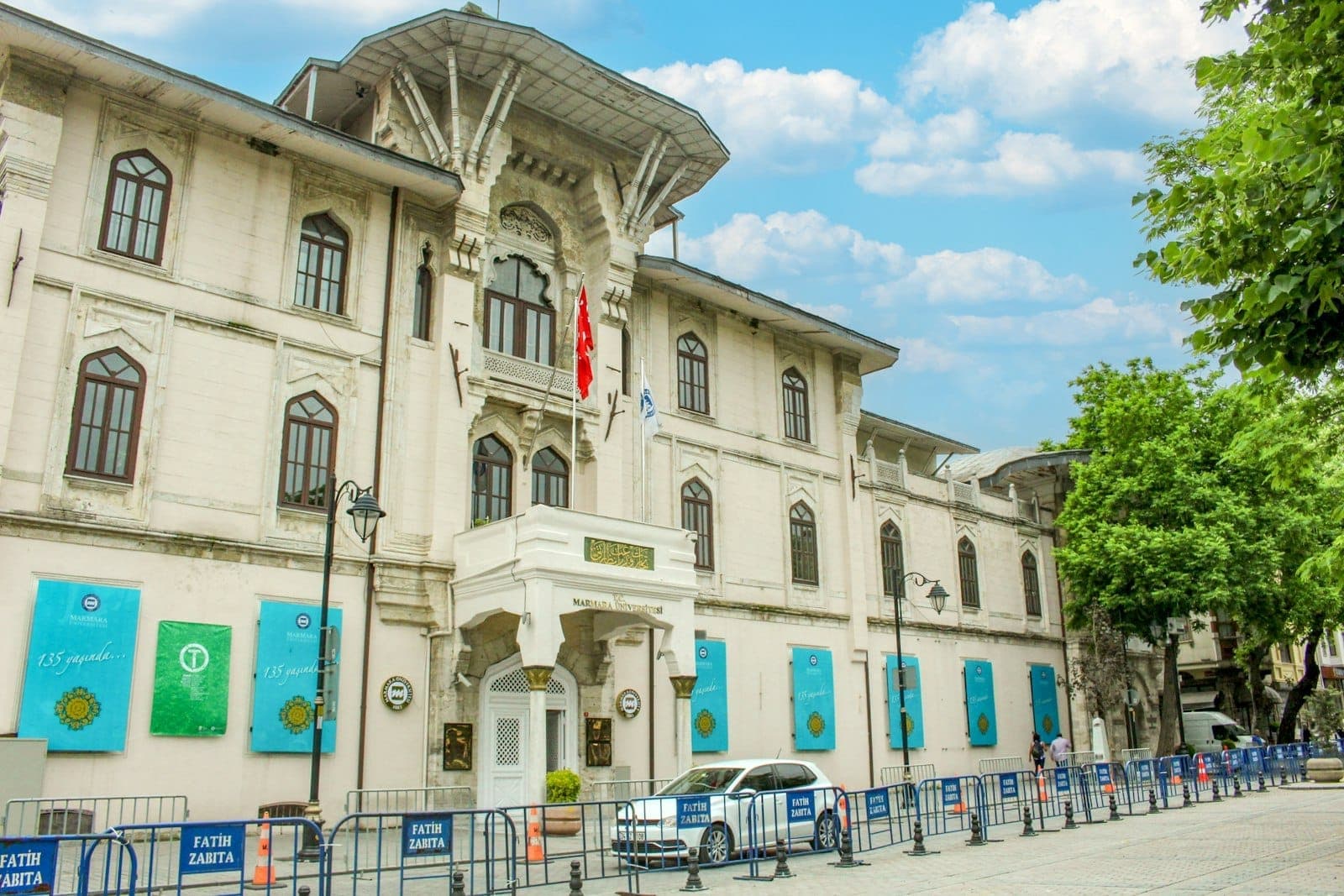 Elegante edificio bianco con striscioni blu e bandiera turca, probabilmente un'importante location di Istanbul, visto sotto un cielo parzialmente nuvoloso.