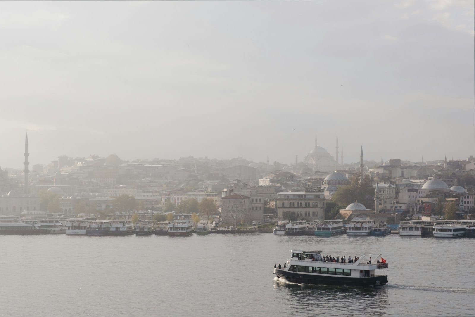 Eine Pendlerfähre überquert den Bosporus mit der Skyline von Istanbul, Moscheen und Kuppeln im Hintergrund bei sanftem Tageslicht.