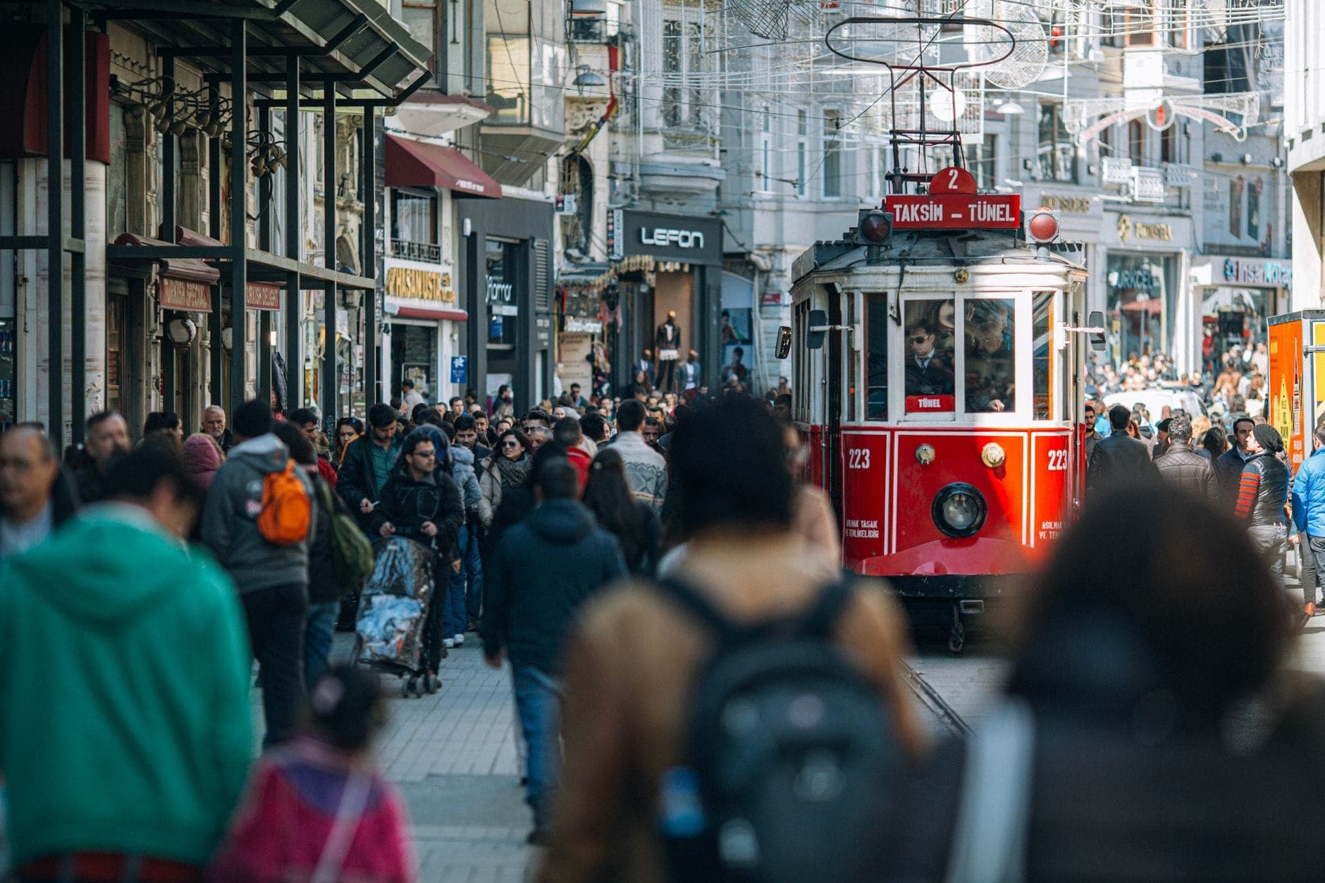 Die belebte İstiklal Caddesi mit der ikonischen roten Nostalgietram, die durch die Menschenmenge fährt, umgeben von historischen Gebäuden und pulsierendem Straßenleben in Istanbul.