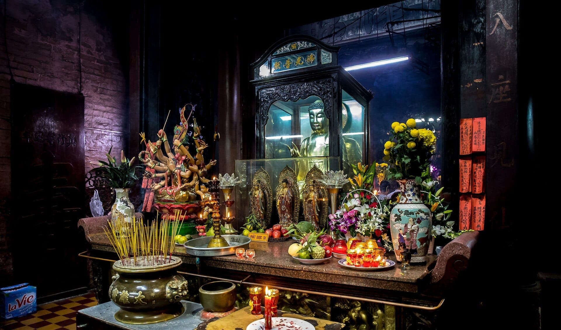 Bàn thờ trang trí cầu kỳ bên trong Chùa Ngọc Hoàng với tượng Phật mạ vàng, que hương, mâm hoa quả, hoa và các tượng thần linh nhiều màu sắc.