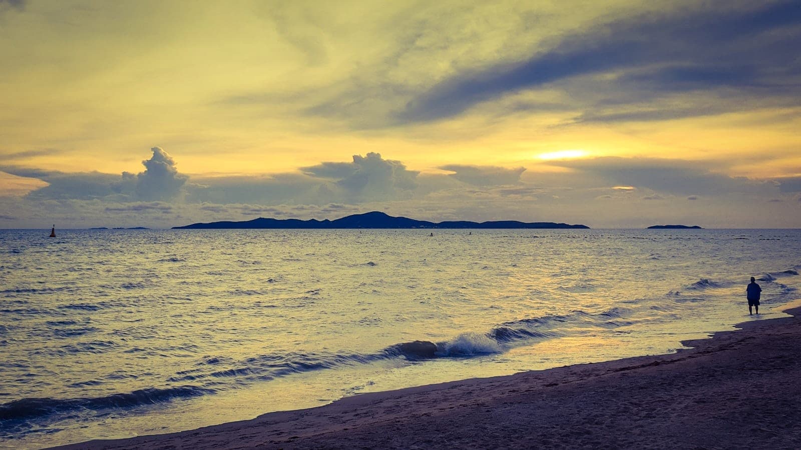 Peaceful Jomtien Beach shoreline at sunset with gentle waves, sandy beach, and a distant solitary figure walking along the water.