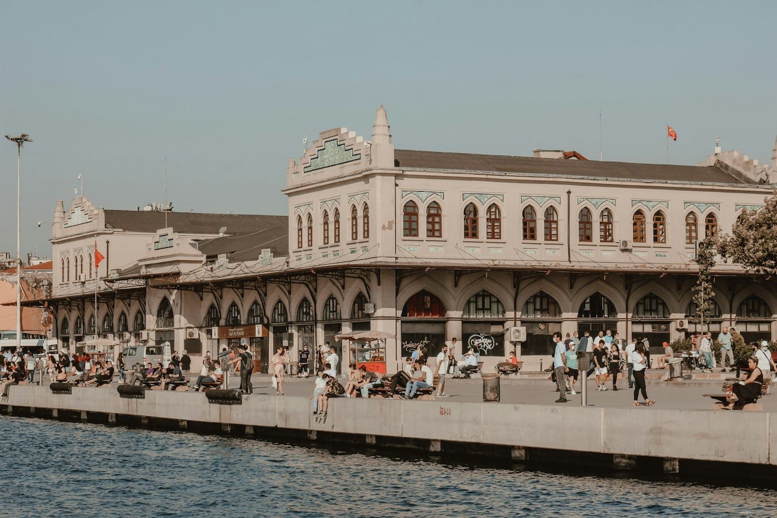 Das belebte Fährterminal von Kadıköy an einem sonnigen Tag am Bosporus – Menschen versammeln sich entlang der Anlegestelle vor dem historischen Fährgebäude.