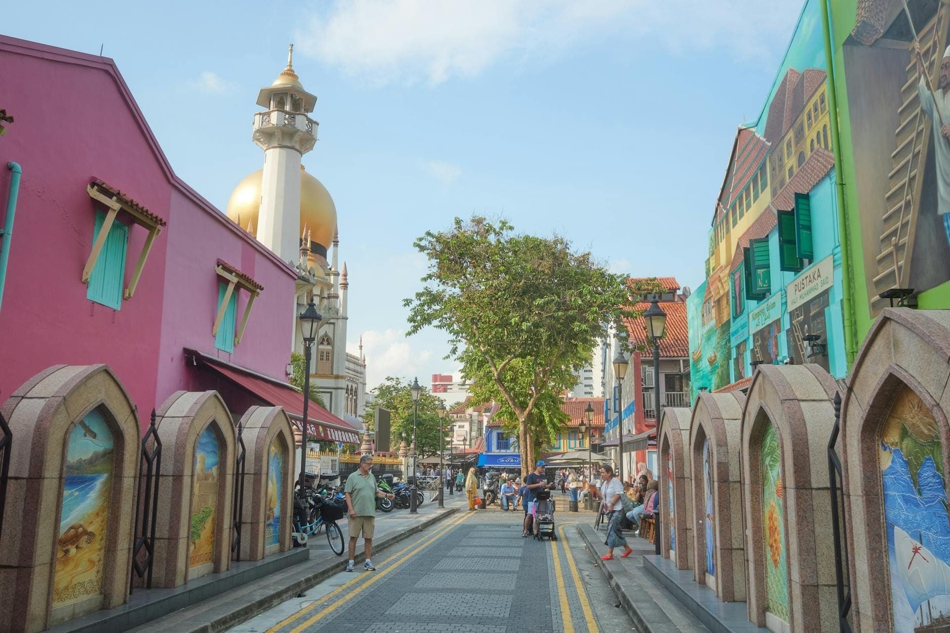 Vibrant street in Kampong Glam with colorful murals, shophouses, and the Sultan Mosque’s golden dome in the background. Pedestrians enjoy the lively, artistic atmosphere.