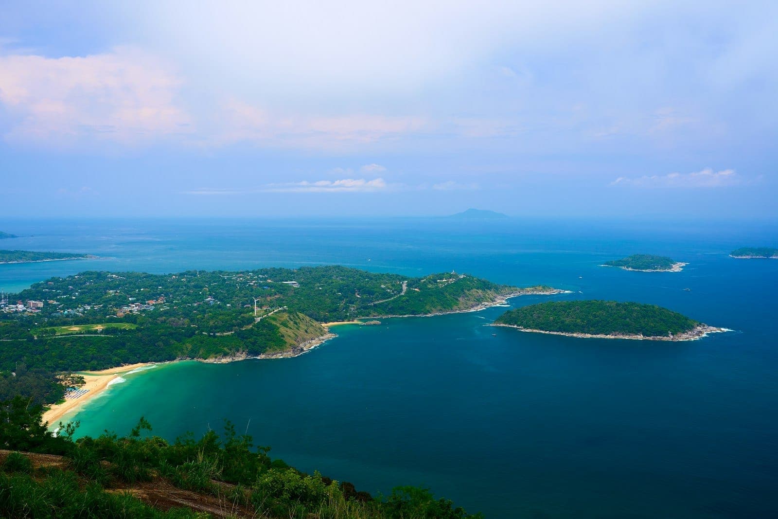 Panoramikong tanaw ng baybayin ng Kata at Karon sa Phuket na may turquoise na dagat, mabuhanging dalampasigan, berdeng burol, at maliliit na isla sa ilalim ng maliwanag na langit.