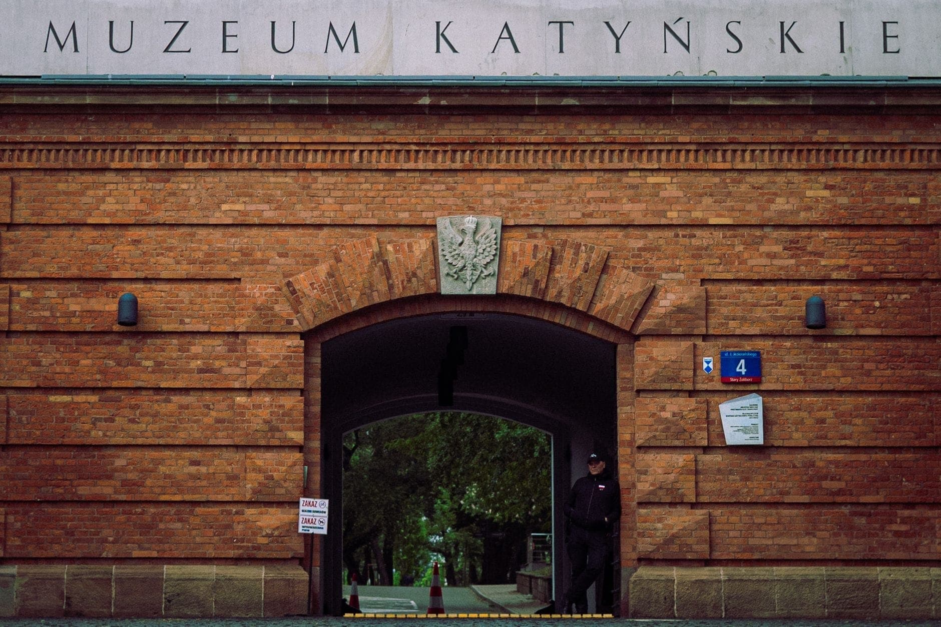 Eingang des Katyń-Museums in der Warschauer Zitadelle: rote Backsteinwände mit dem Schriftzug 'Muzeum Katyńskie' über einem Rundbogentor, davor ein einzelner Wachposten.