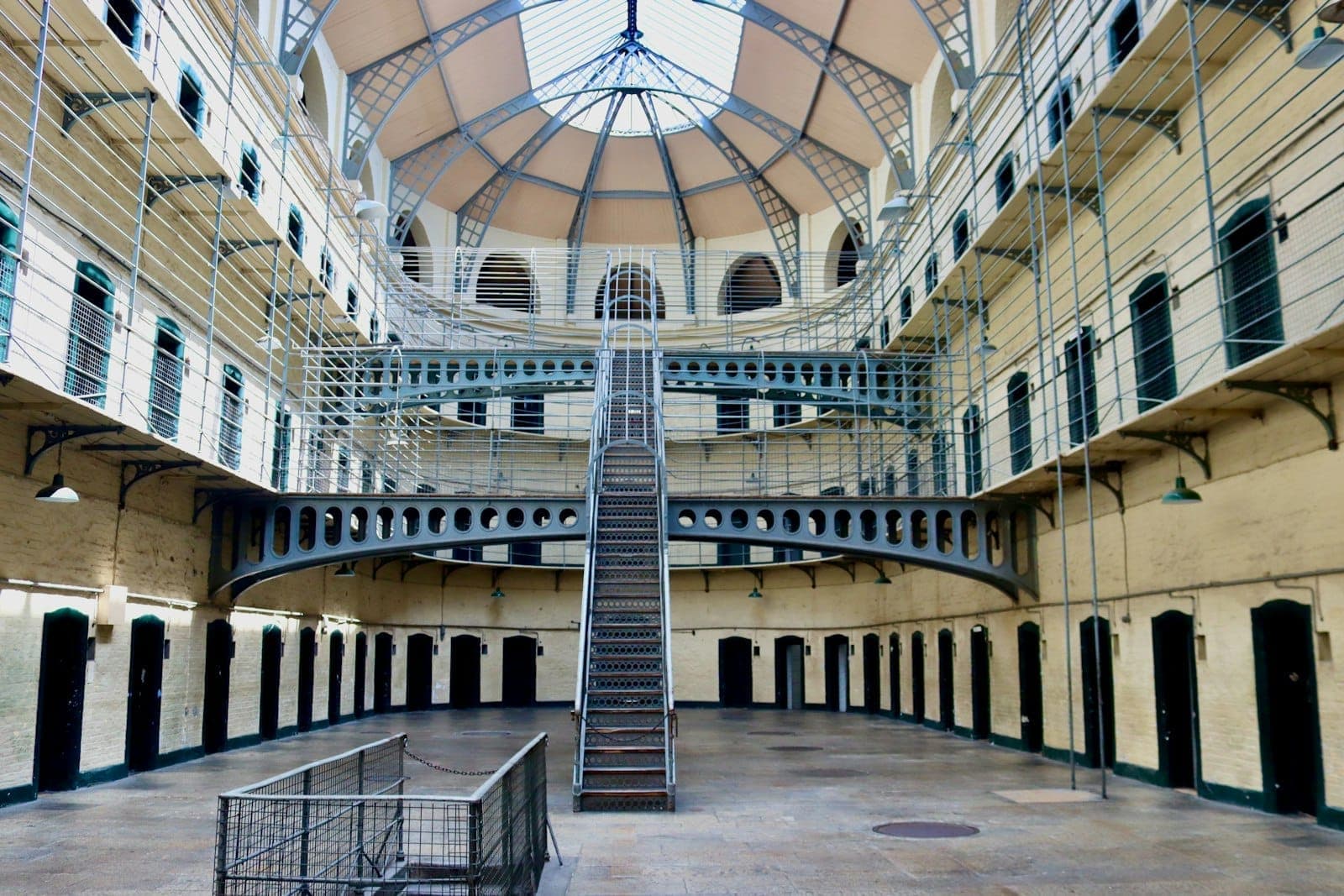 Das helle, weiträumige Innere des Kilmainham Gaol mit einer zentralen Treppe, Metallgalerien und Gewölbedecken im Tageslicht.