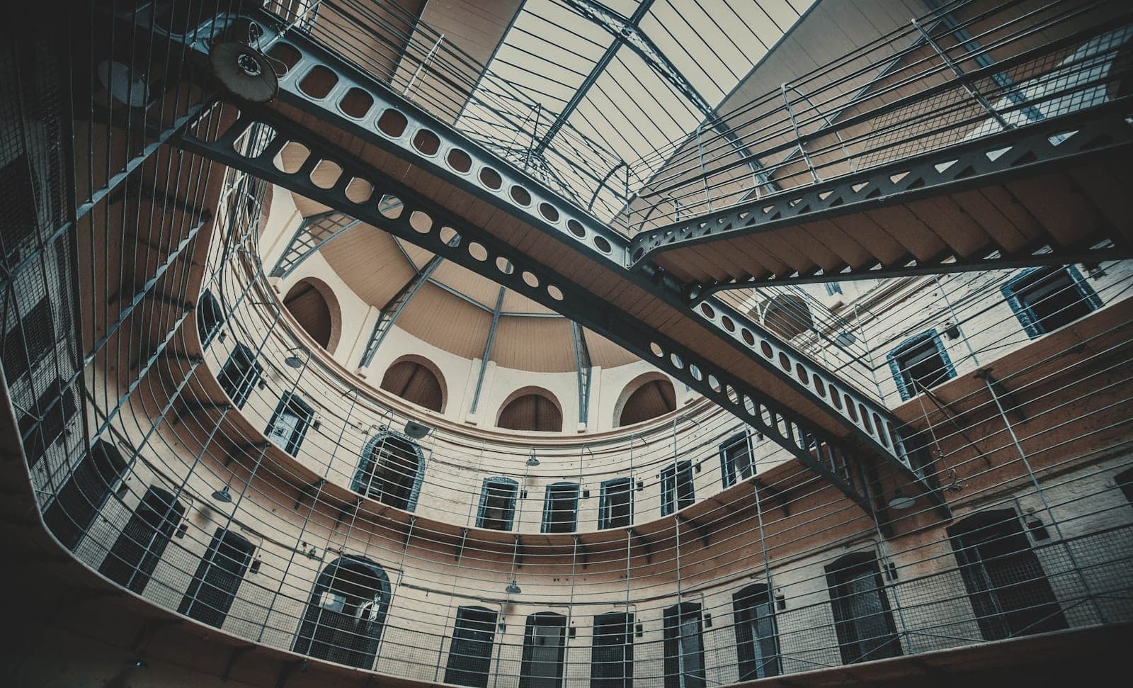 Widok wnętrza Kilmainham Gaol Museum z wiktoriańskimi żelaznymi pomostami, wieloma drzwiami cel i kopułowym sufitem z przeszklonym świetlikiem.