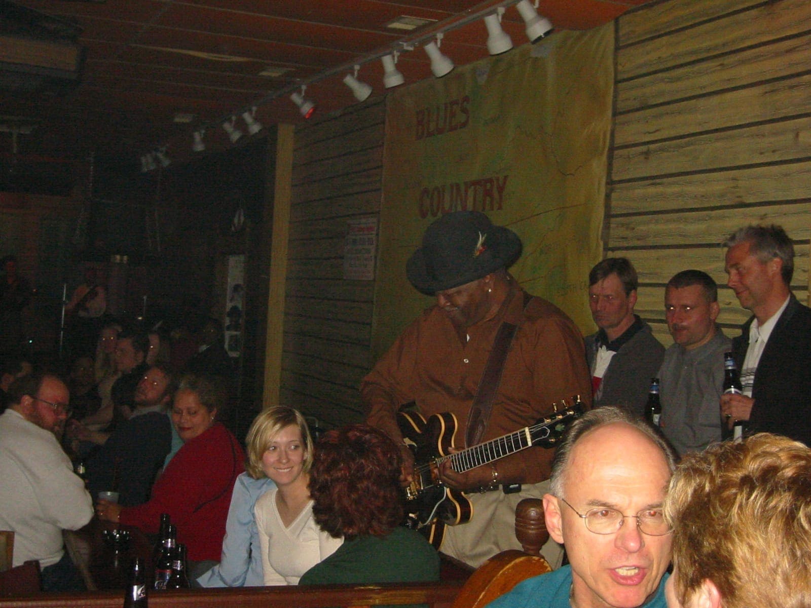 Ein Bluesmusiker spielt E-Gitarre im Kingston Mines, umgeben von einem lebhaften Publikum in einem gemütlichen, schwach beleuchteten Club.
