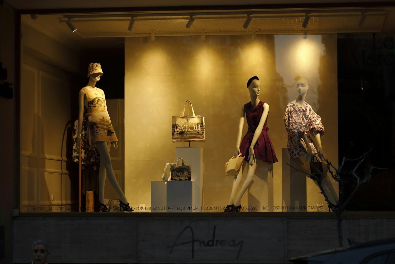 Chic boutique window display with three stylish mannequins dressed in luxury fashion, well-lit and inviting, reflecting Kolonaki’s upscale shopping vibe in Athens.