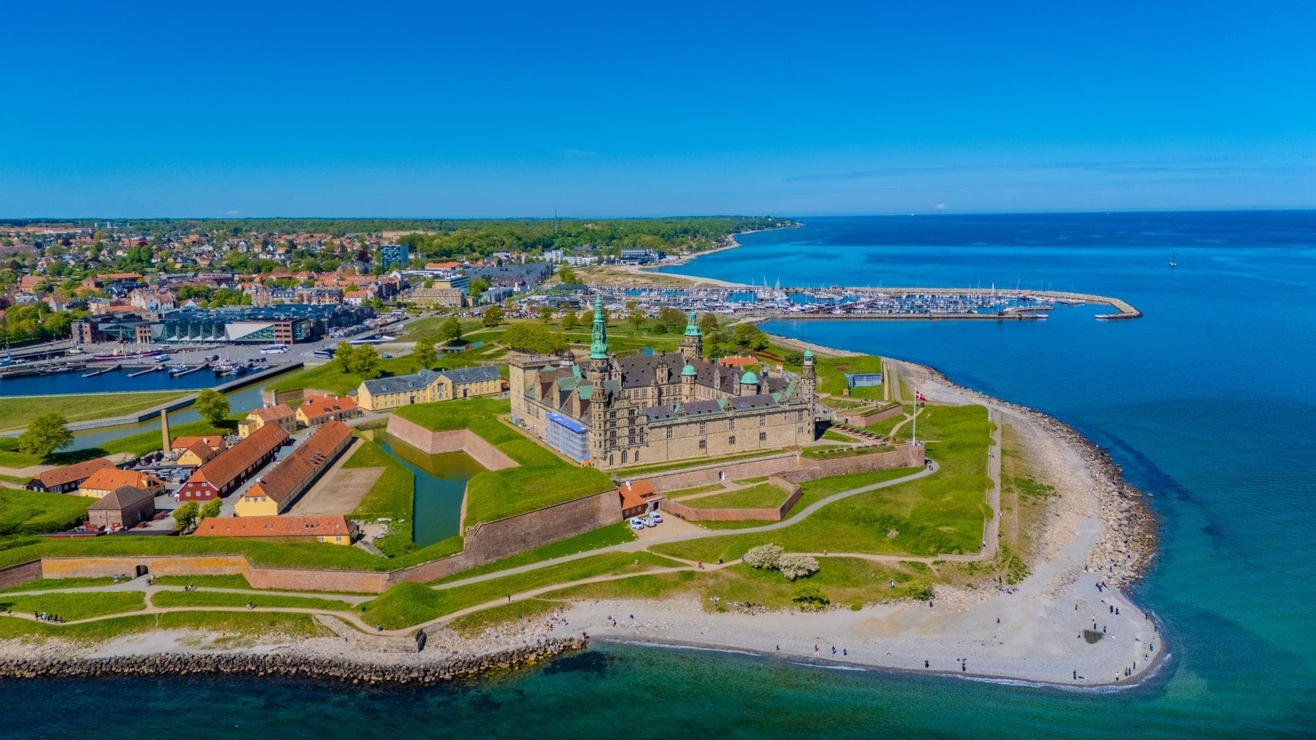 Una splendida vista aerea del Castello di Kronborg in una giornata di sole, circondato dall'acqua, dalle verdi fortificazioni e dalla città di Helsingør sullo sfondo.