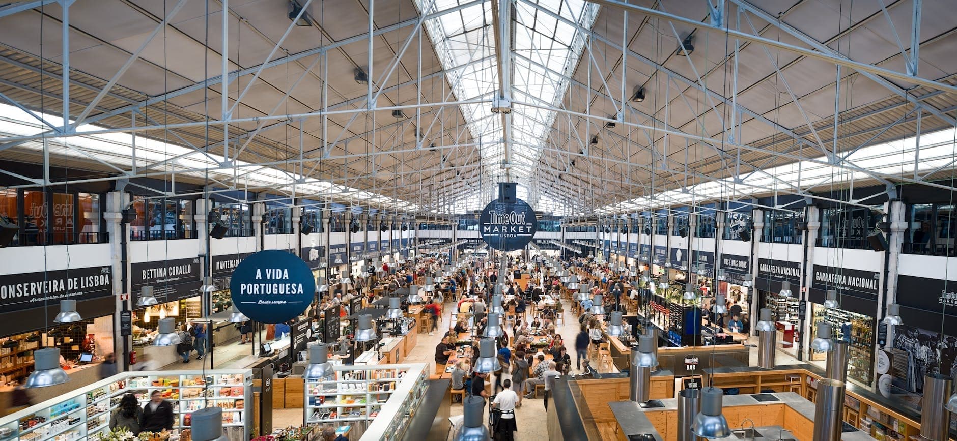 Khu chợ trong nhà tấp nập ở Lisbon với nhiều gian hàng nhộn nhịp bên dưới mái kính cao, không khí mua sắm đô thị sôi động.