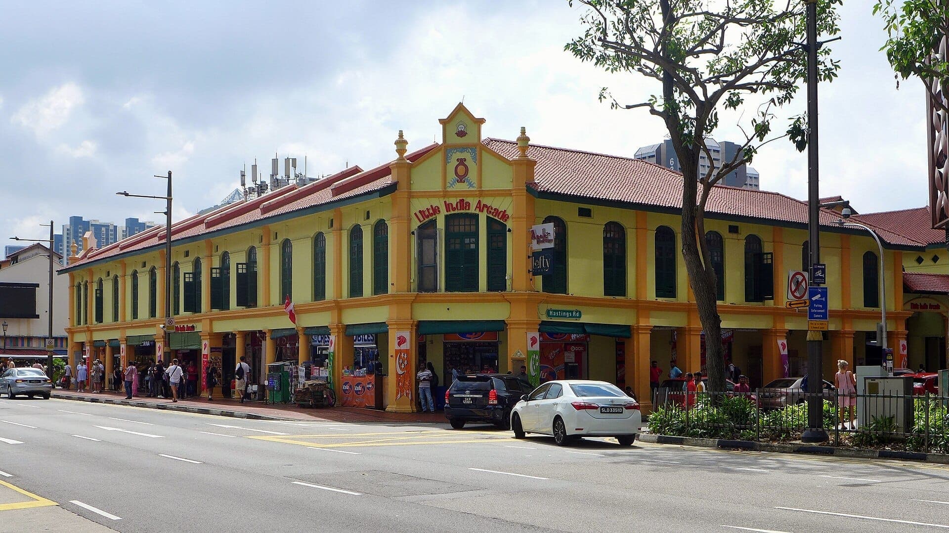 The yellow and orange colonial shophouse exterior of Little India Arcade, with green windows and visitors walking along Serangoon Road in Singapore.