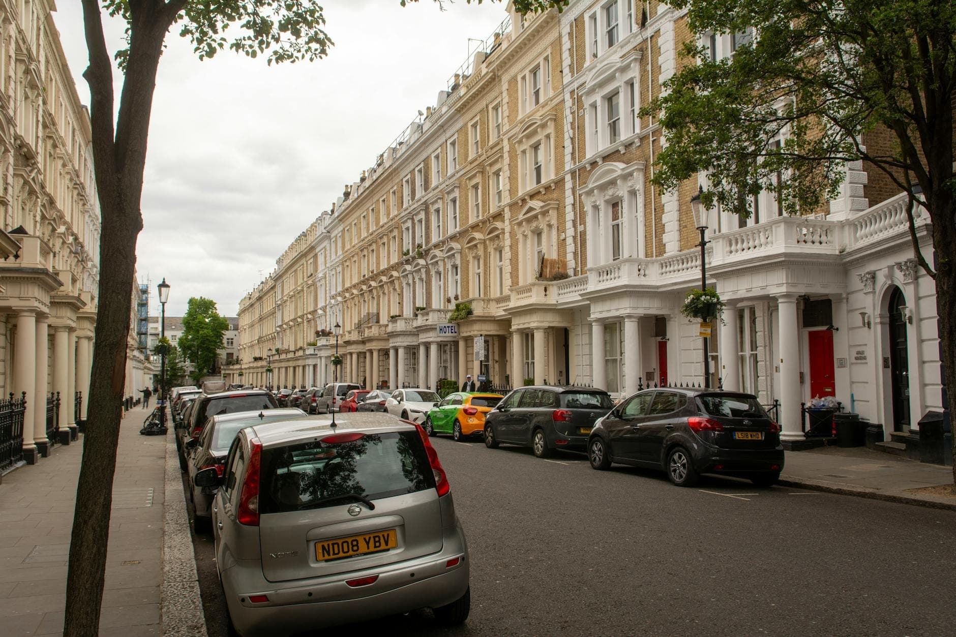 Street in London showing rows of classic terraced townhouses with parked cars and trees, typical accommodation options for visitors.