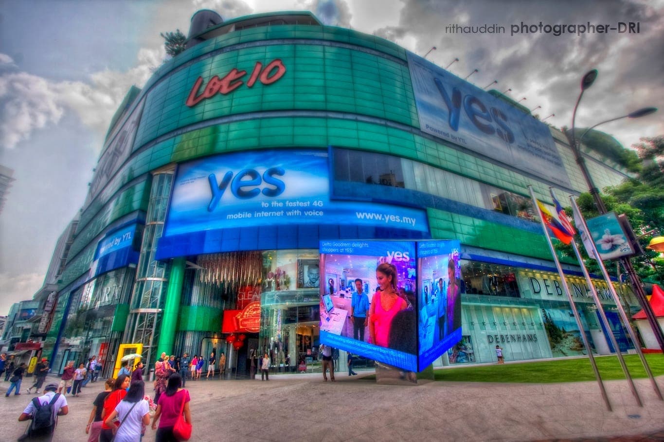 Mặt ngoài của Trung tâm mua sắm Lot 10 tại Bukit Bintang nổi bật với mặt tiền kính cong, các biển quảng cáo kỹ thuật số rực rỡ và đám đông tụ tập gần lối vào chính.