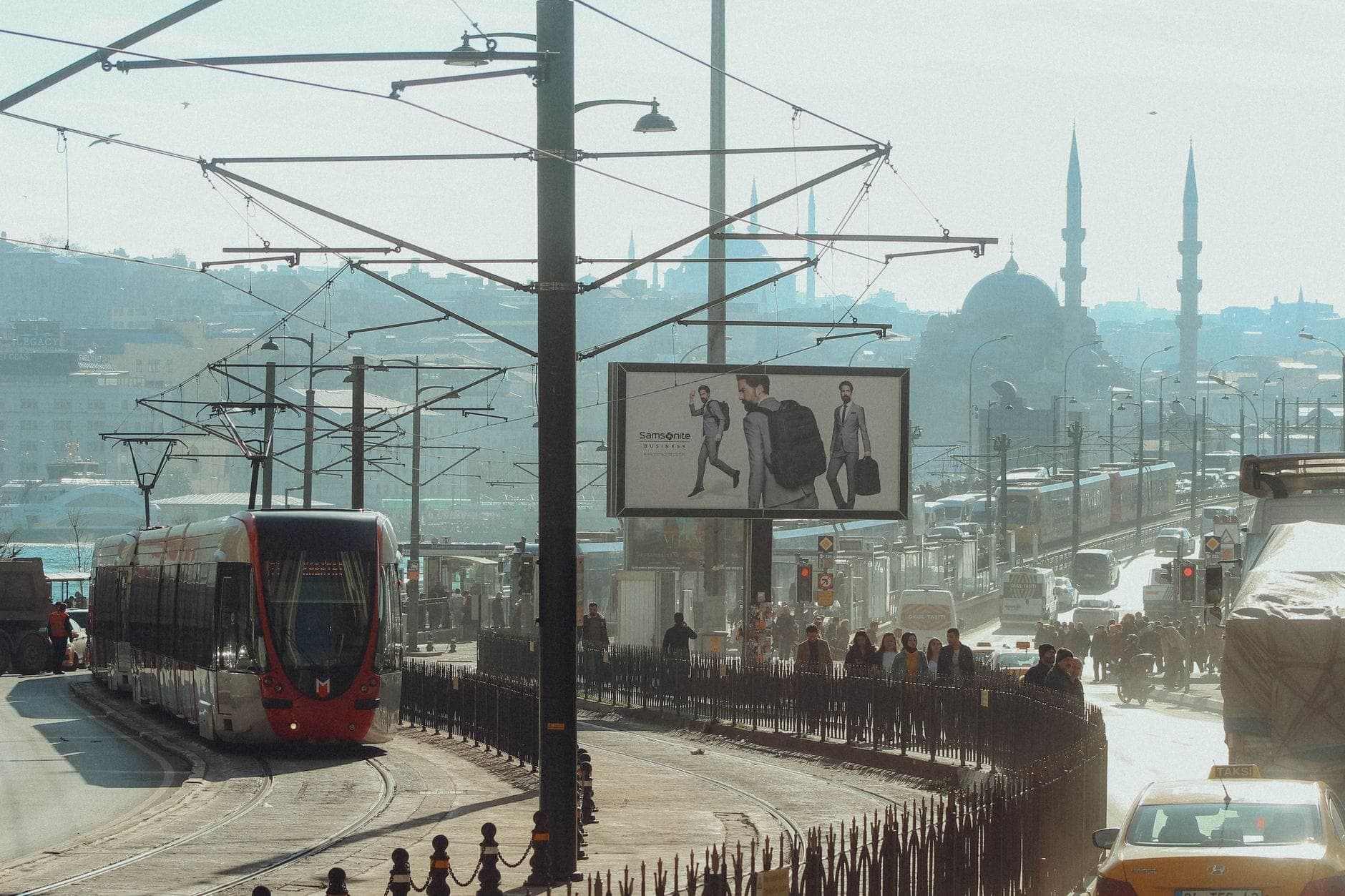 Tranvía moderno cruzando el Puente de Gálata en Estambul con mezquitas históricas y el horizonte de la ciudad al fondo, escena urbana diurna.