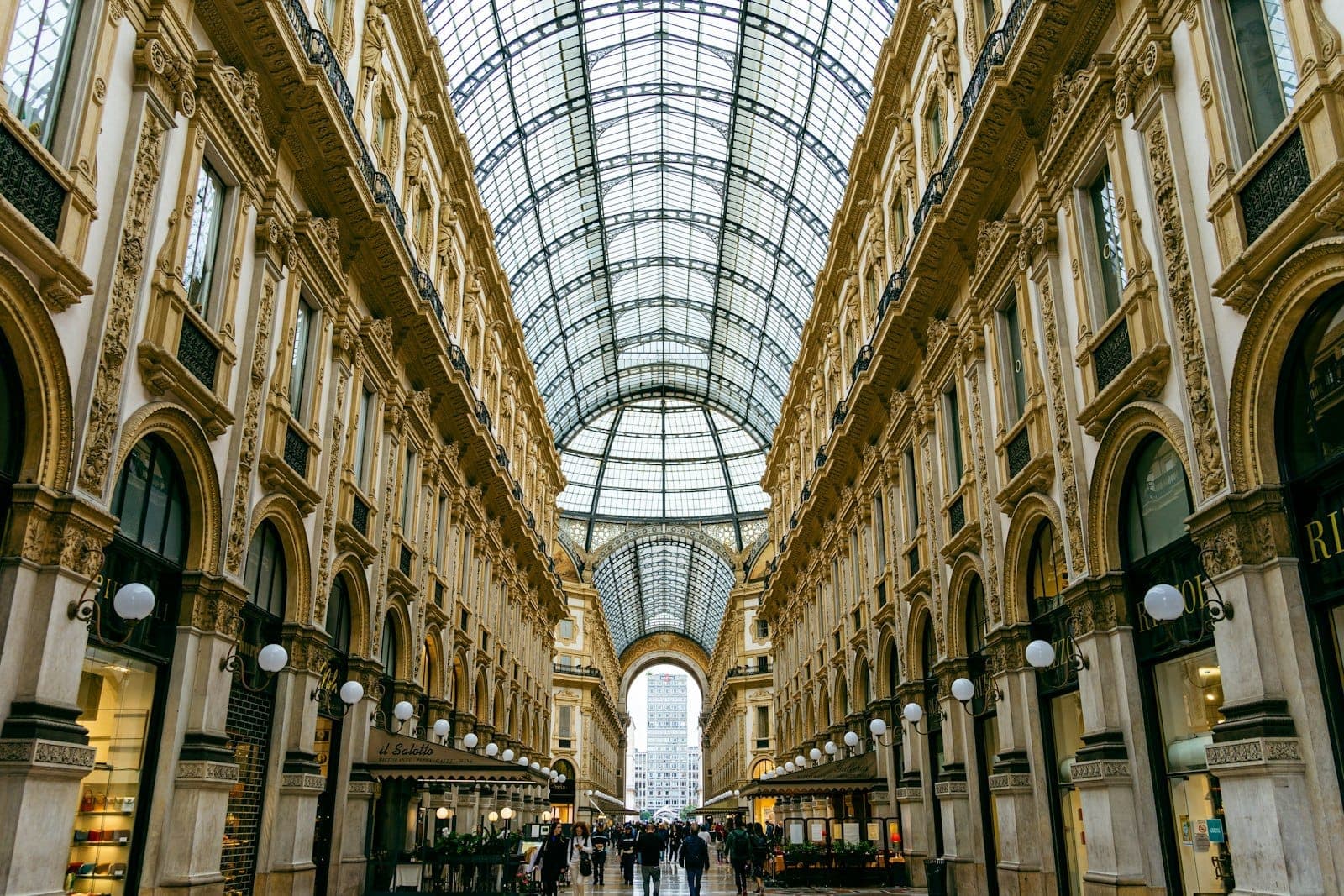 Wide angle view of Milan’s luxurious Galleria Vittorio Emanuele II, featuring ornate arches, elegant shops, and a soaring glass roof full of light.