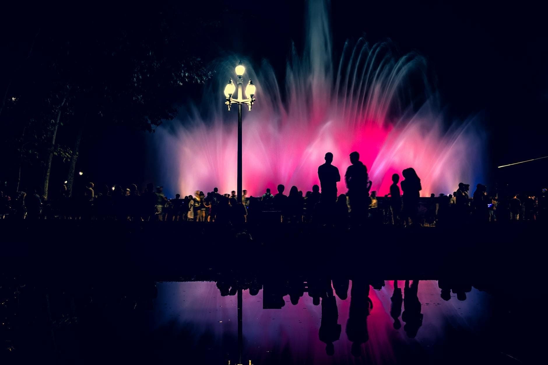 Đám đông in bóng trước Font Màgica de Montjuïc rực rỡ ánh đèn về đêm, những tia nước đầy màu sắc phản chiếu lung linh tạo nên không khí lễ hội sôi động.