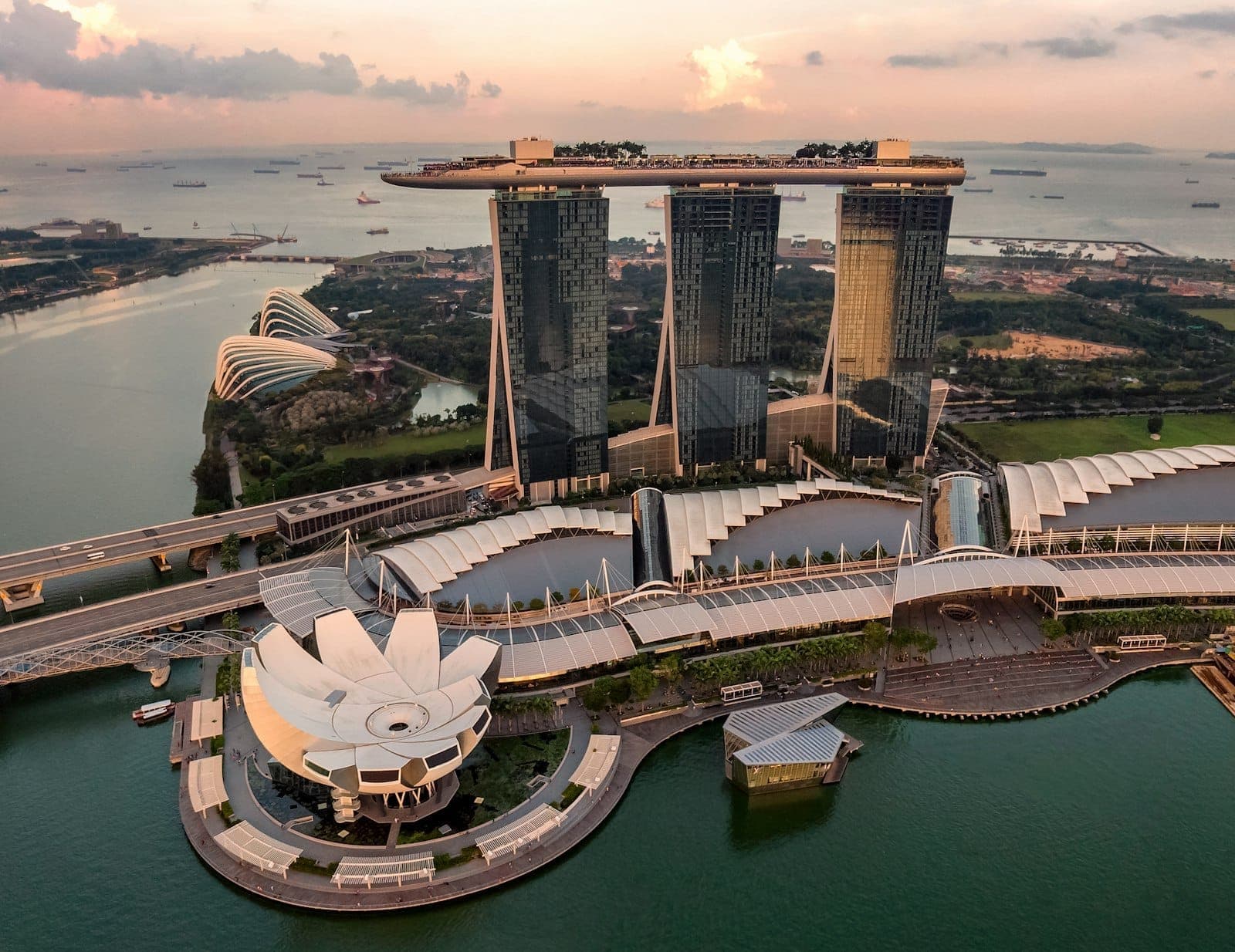 Aerial view of Marina Bay Sands in Singapore at sunset with the SkyPark, ArtScience Museum, and surrounding bay area, showcasing the city’s iconic skyline and water.