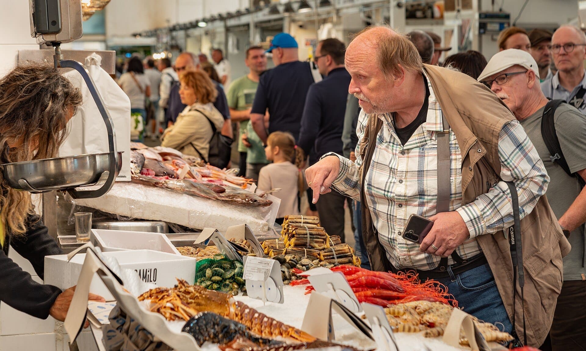 Quầy hải sản tấp nập tại Mercado Central de Abastos ở Cádiz, với nhiều người đang xem cá tươi, hải sản và đặc sản địa phương dưới ánh đèn chợ sáng rực.
