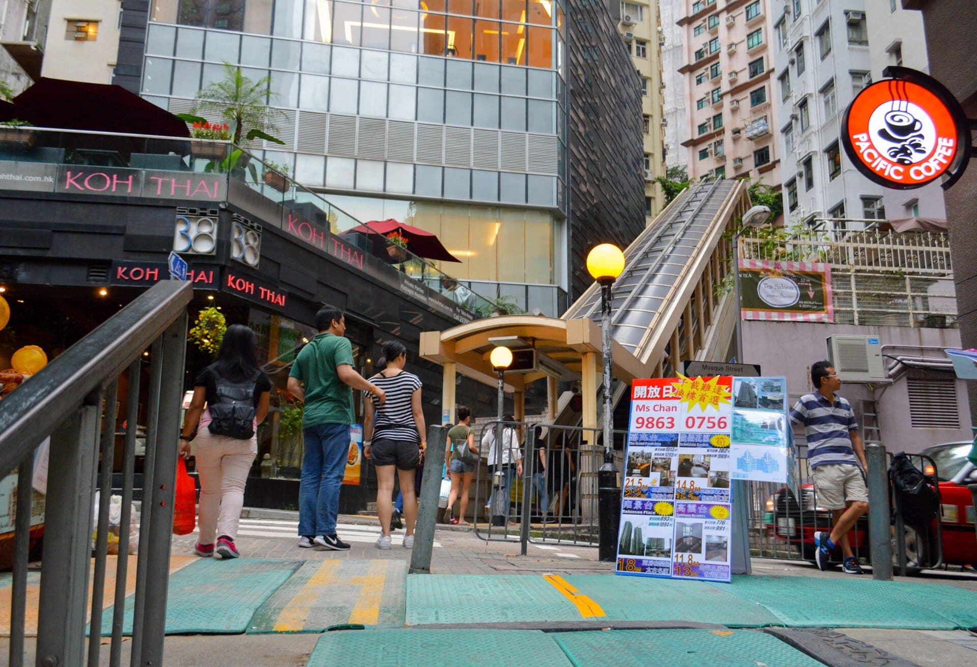Lối vào đông đúc của thang cuốn Mid-Levels tại Hong Kong với các tòa nhà đô thị và góc nhìn từ mặt đường vào ban ngày.