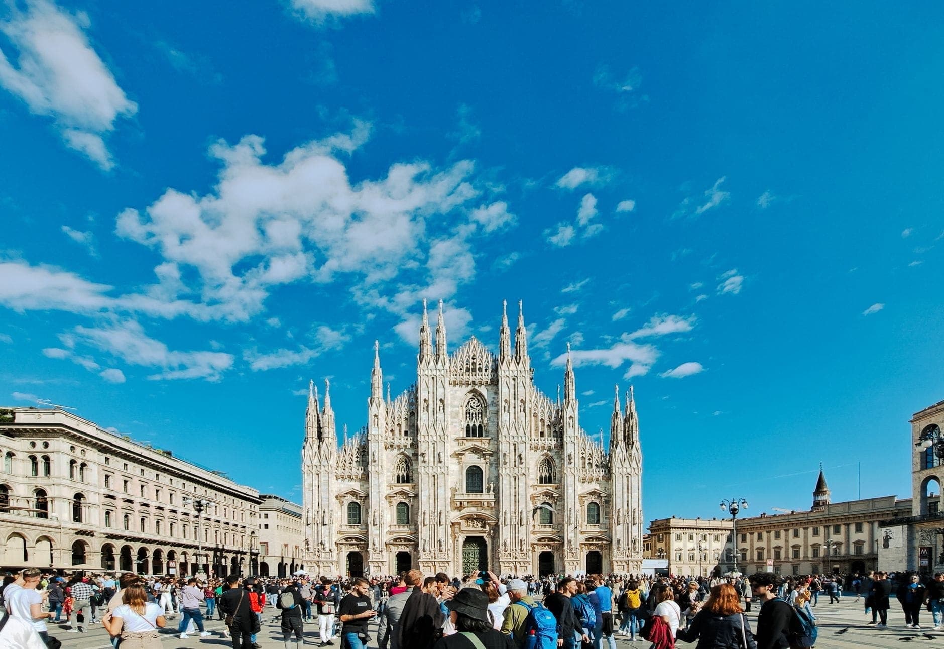 Folle di persone davanti al Duomo di Milano sotto un cielo azzurro, a indicare un periodo di grande affluenza in città.