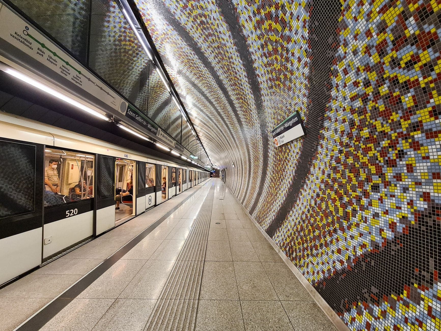 Moderna stazione della Metro di Milano con caratteristico mosaico a parete e treno della linea M4 in arrivo al binario.