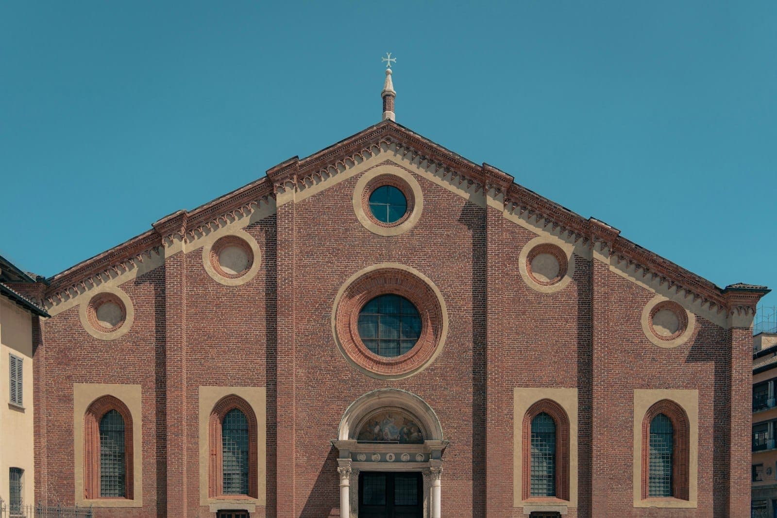 Fassade von Santa Maria delle Grazie in Mailand, eine Renaissancekirche aus rotem Backstein mit dekorativen Bögen unter klarem Himmel.