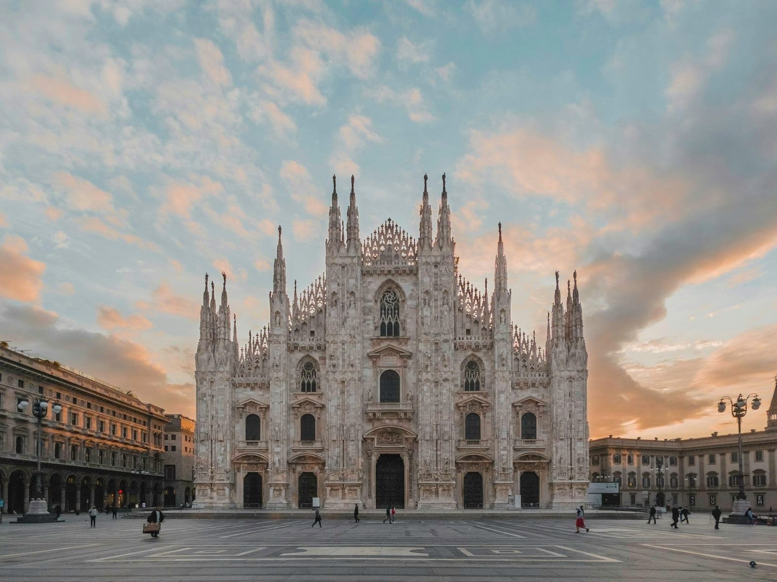 Front view of Milan Cathedral (Duomo di Milano) at sunrise with dramatic sky, empty main square, and beautiful Gothic architecture.