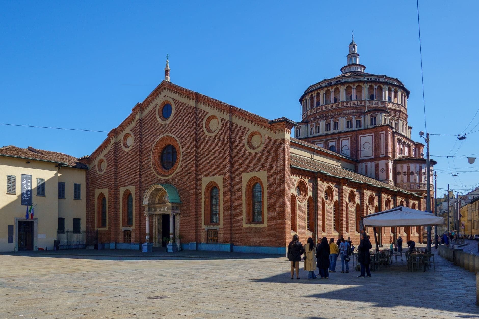 Ampia veduta di Santa Maria delle Grazie a Milano, con la sua facciata rinascimentale in mattoni e l'iconica cupola in una giornata di sole.