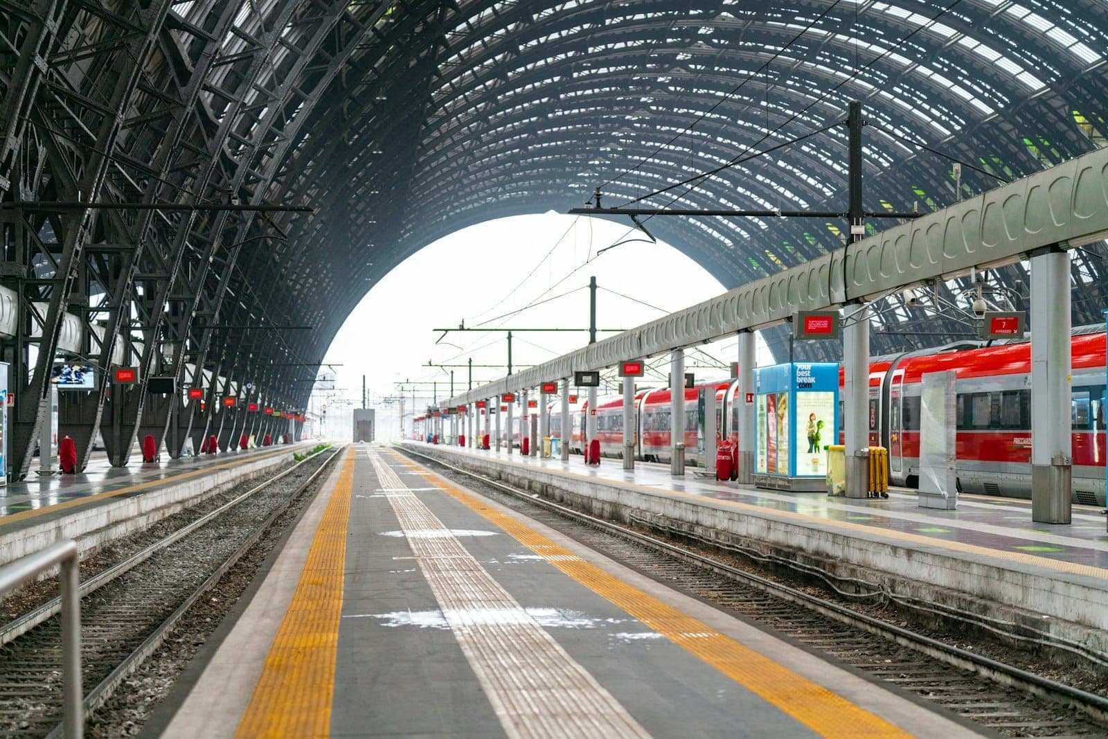 Weitblick auf die Bahnsteige des Bahnhofs Milano Centrale mit roten Zügen und gewölbtem Glasdach, ein ikonischer Verkehrsknotenpunkt für Reisen durch Mailand.