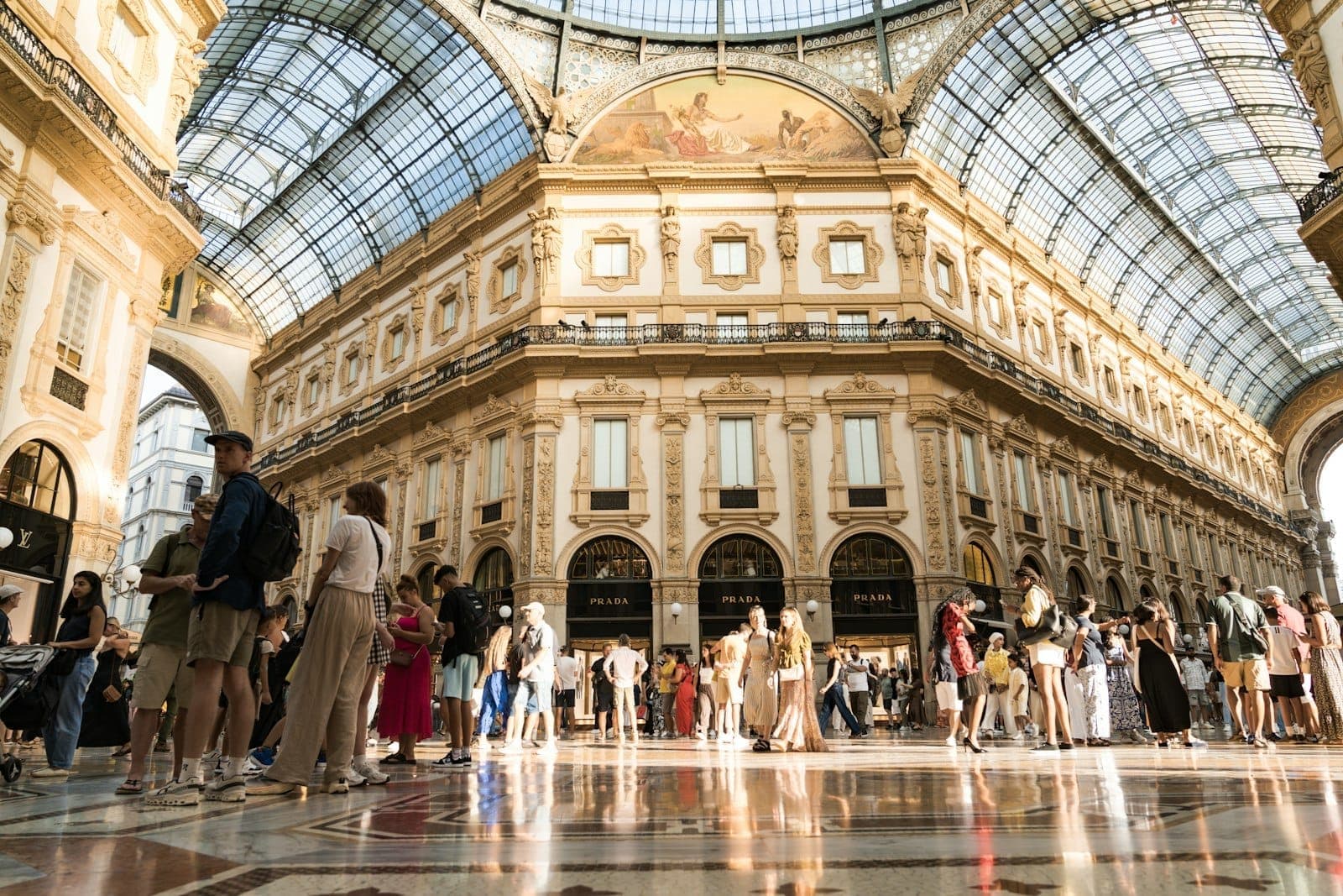 Wide view of Milan’s Galleria Vittorio Emanuele II filled with stylish shoppers under a grand glass ceiling on a sunny day.