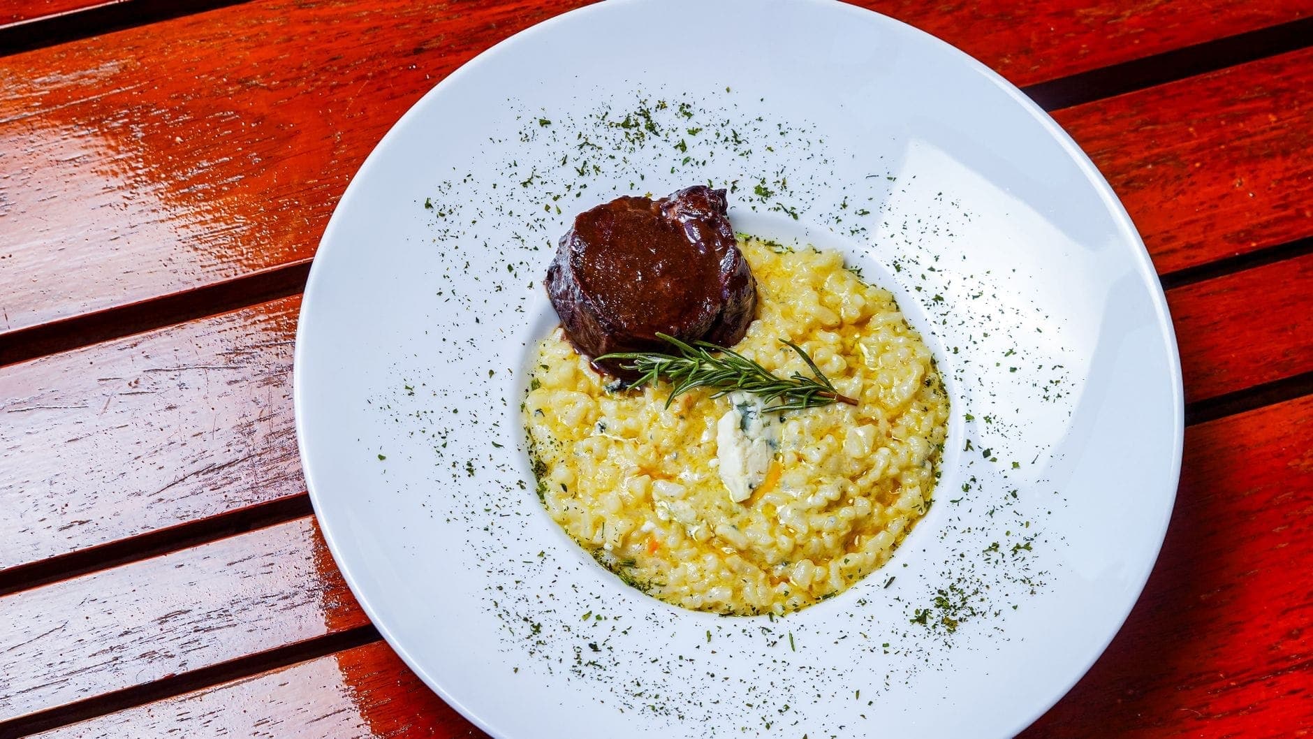 Un piatto di risotto alla milanese dorato con erbe aromatiche e carne, servito su un tavolo di legno in un ristorante.
