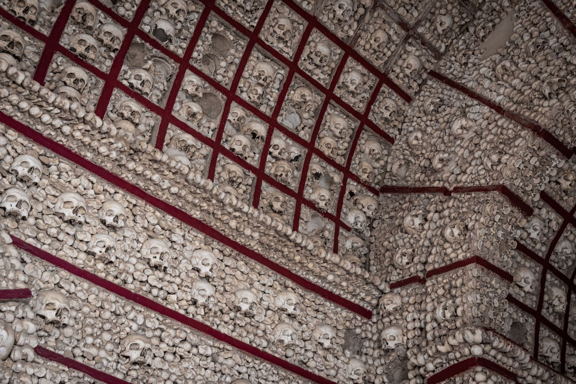 Wand aus menschlichen Schädeln und Knochen in einem geometrischen Rastermuster, das auf ein historisches Ossarium oder eine Krypta hindeutet.