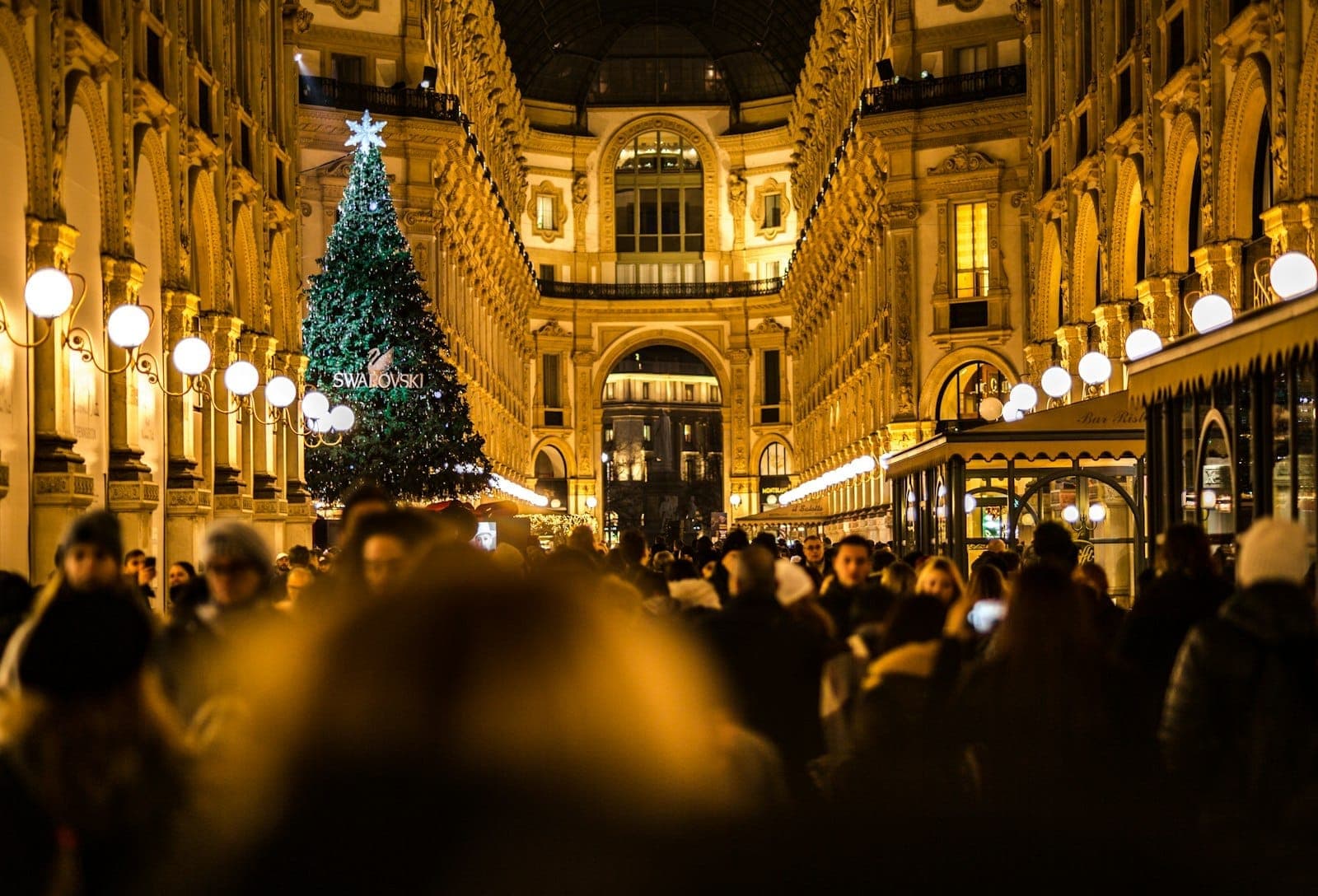 Crowds enjoy festive atmosphere at Milan’s Galleria Vittorio Emanuele II, featuring a large Christmas tree and glowing holiday lights at night.