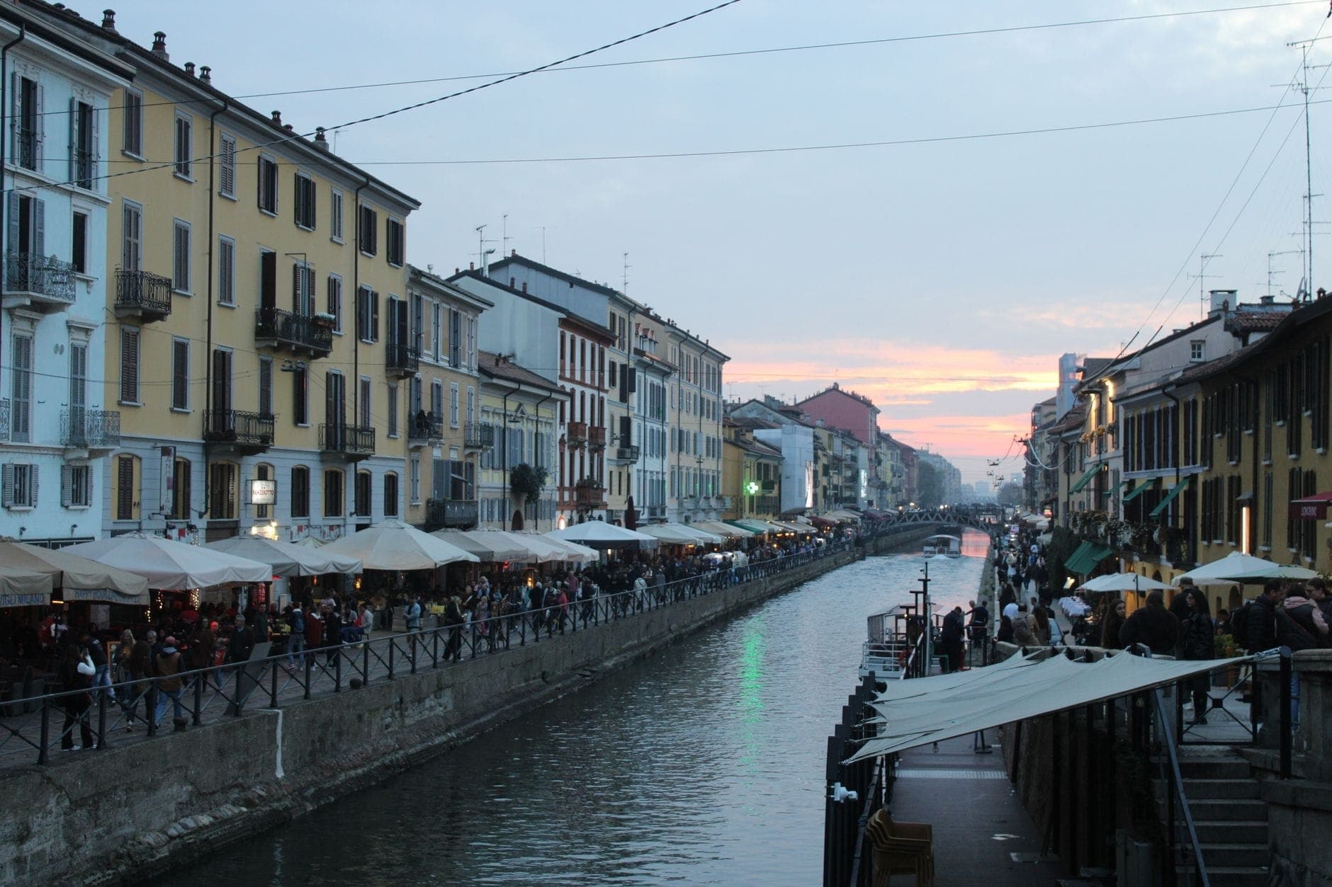 Belebte Kanalstraße bei Sonnenuntergang im Navigli-Viertel von Mailand mit lebhaften Bars und Menschen, die den Abend genießen.