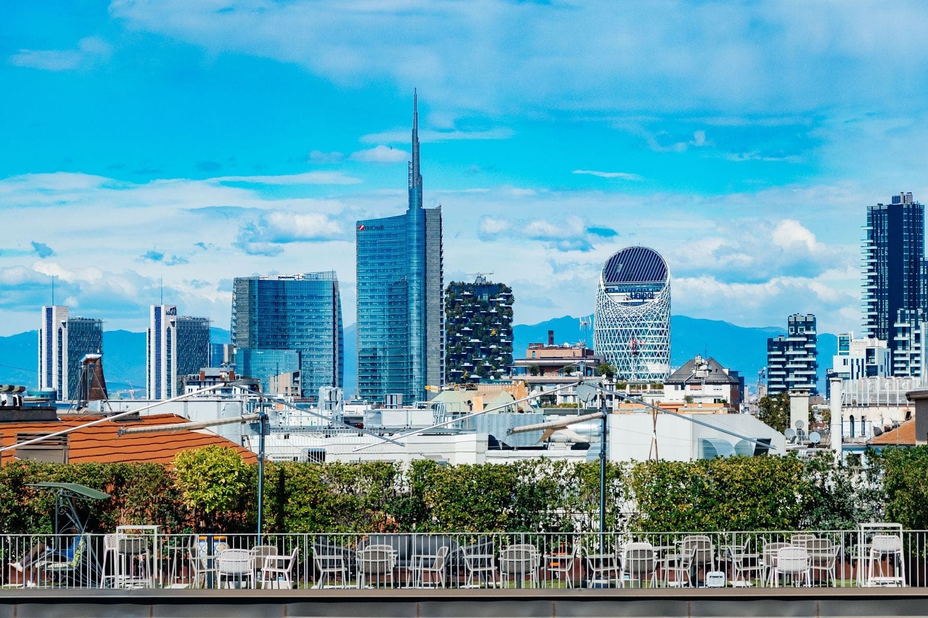 Dachterrasse mit Tischen und Stühlen mit Blick auf die Skyline von Mailands Porta Nuova und die Wolkenkratzer an einem hellen Tag.