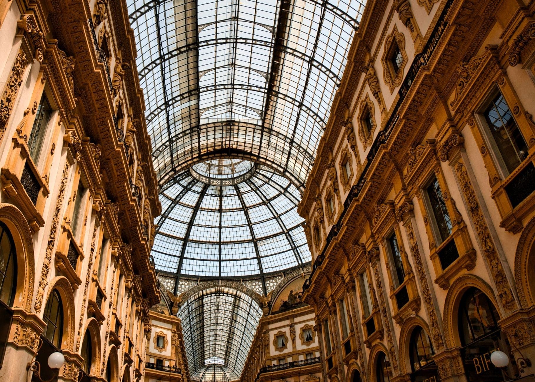 Szerokokątny widok na ozdobną galerię handlową Galleria Vittorio Emanuele II ze szklanym dachem w Mediolanie, ukazujący elegancką architekturę i ogólnodostępną przestrzeń.