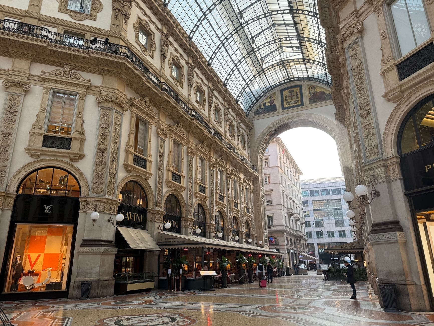 Elegant interior of the Galleria Vittorio Emanuele II in Milan with luxury shops, ornate architecture, and natural light streaming through the glass roof.