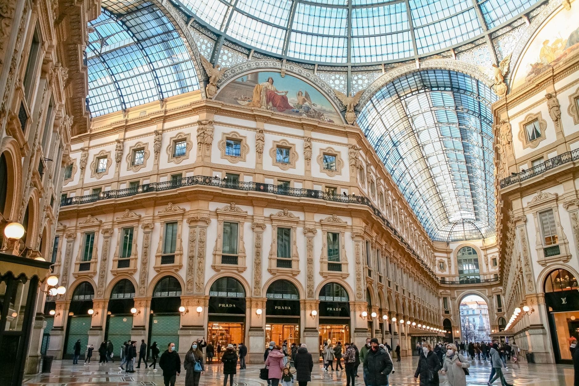 Personas caminando dentro de la ornamentada Galleria Vittorio Emanuele II en Milán, bajo su gran cúpula de cristal y la intrincada arquitectura del siglo XIX.