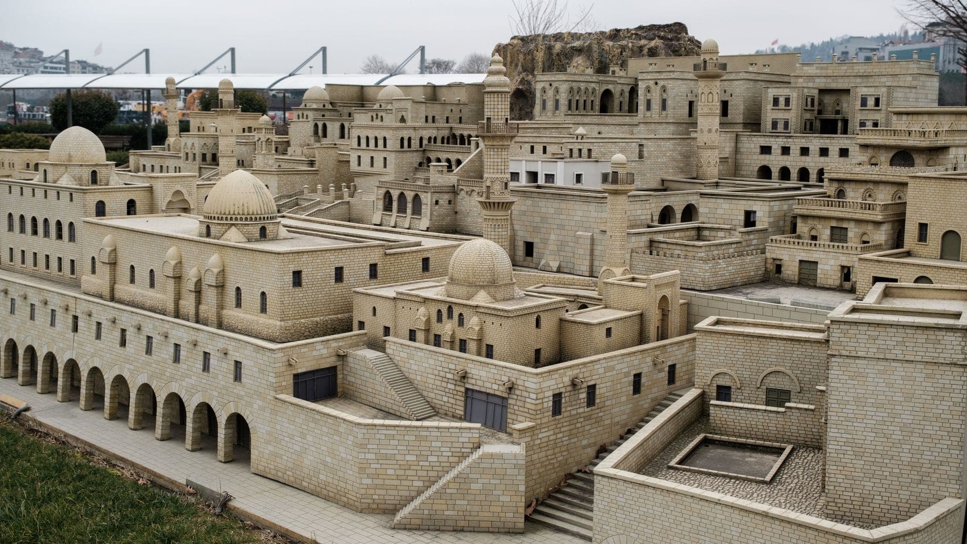 Weitläufiger Blick auf detaillierte Miniatur-Steinbauten im Miniatürk, die türkische Architekturdenkmäler in einem Freiluftpark mit Rasenflächen und Strukturen im Hintergrund zeigen.